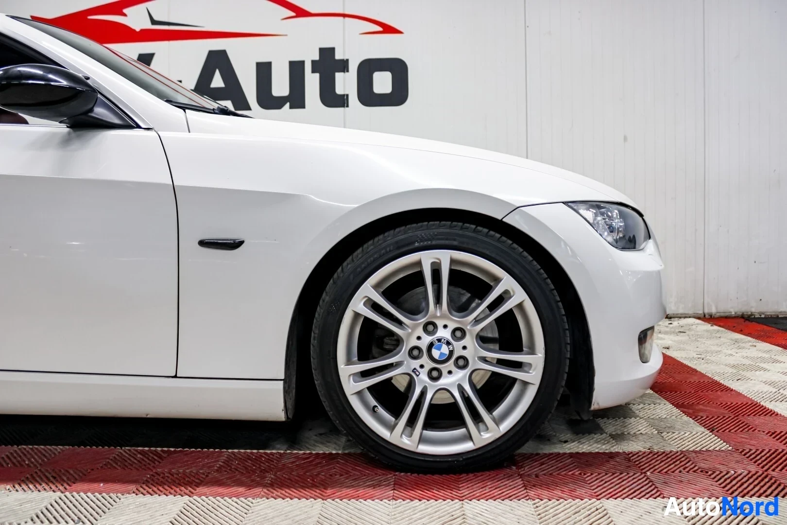 Yksityiskohta: Lähikuva valkoisen auton vasemmasta eturenkaasta ja valkoisesta vanteesta, jossa BMW-logo.