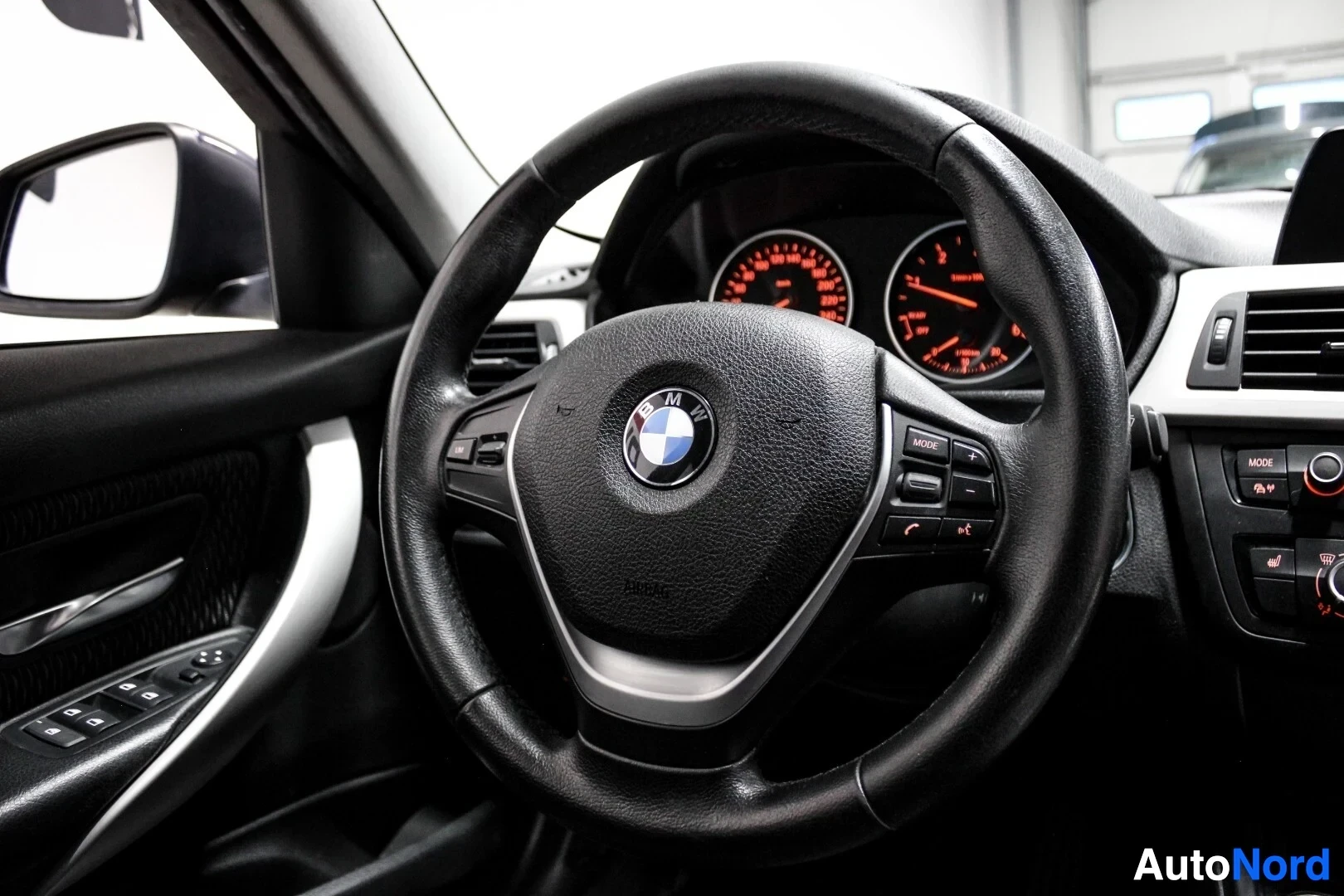 Ohjaamo: Lähikuva ohjauspyörästä, jossa on keskellä BMW-logo ja monitoiminäppäimet.