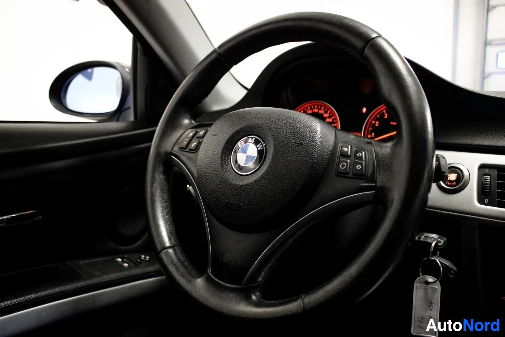 Yksityiskohta: Lähikuva ohjauspyörästä, jossa BMW-logo ja monitoiminäppäimet, sekä osittain näkyvä mittaristo ja kuljettajan oven paneeli.