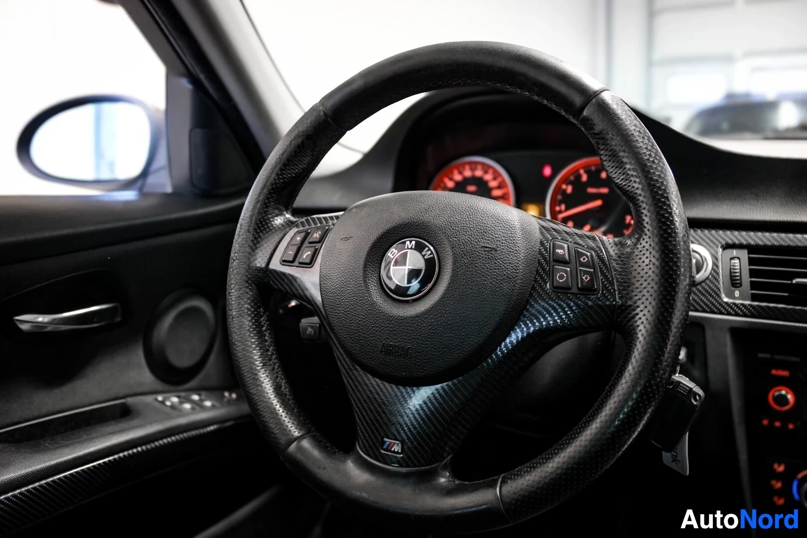 Yksityiskohta: Lähikuva ohjauspyörästä, jossa on BMW-logo keskellä ja monitoimipainikkeet ohjauspyörän puolissa.