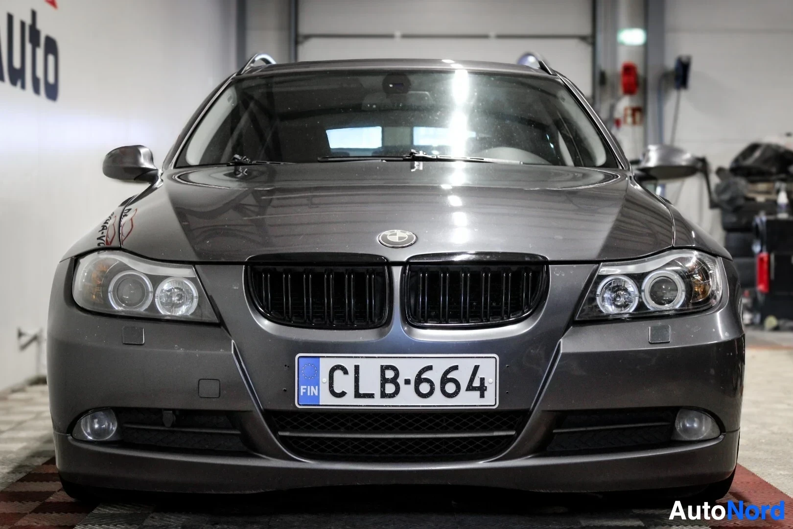 Edestä: BMW 3-sarjan Touringin etuosa autohallissa. Autossa on mustat säleiköt ja ajovalot.