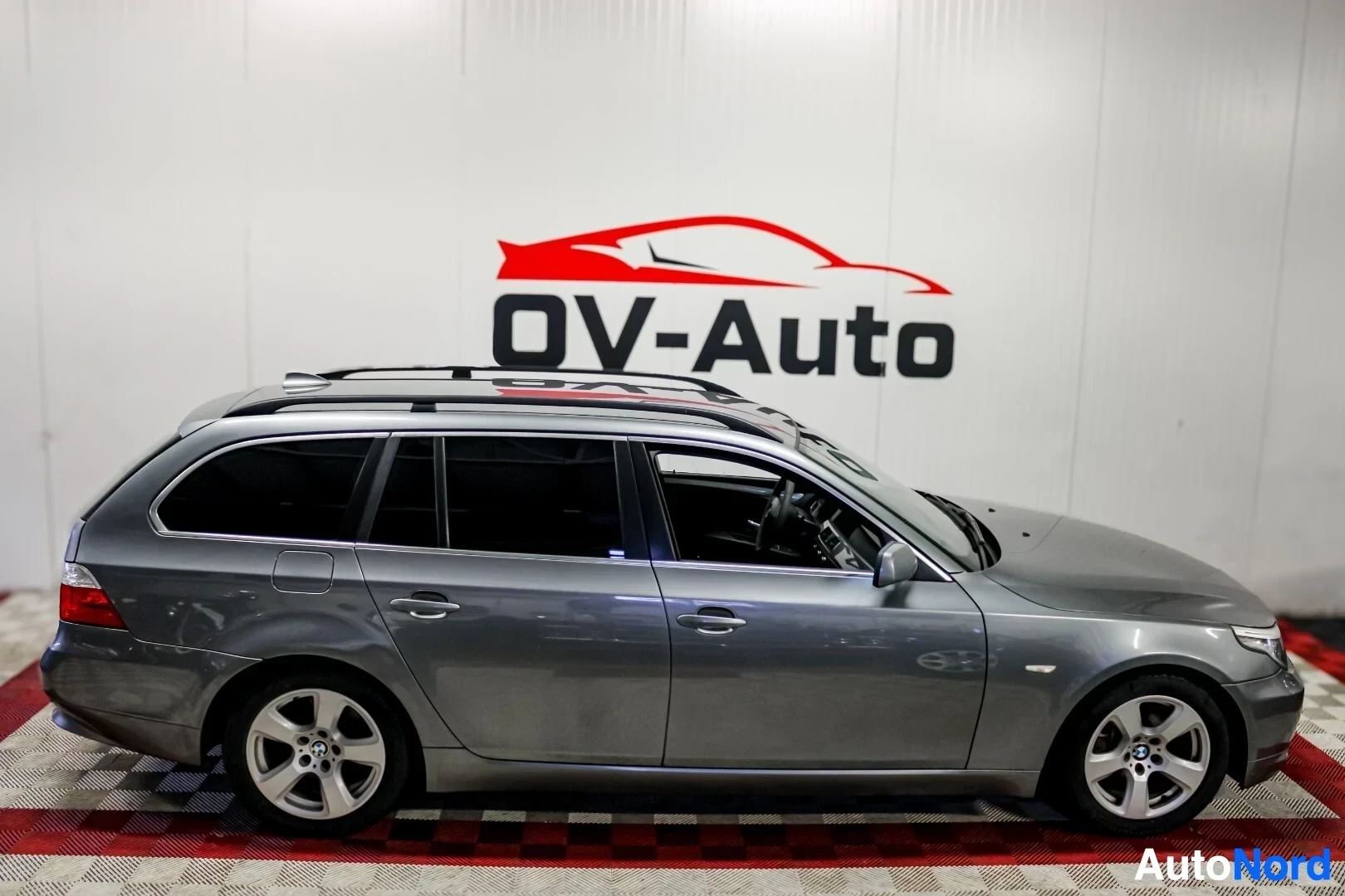 Sivulta: Harmaa BMW 530d Touring -farmariauto kuvattuna suoraan oikealta sivulta. Autossa on kattokaiteet ja kevytmetallivanteet.