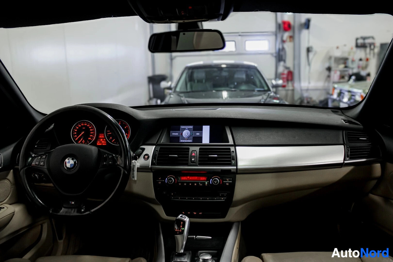 Ohjaamo: Ohjaamonäkymä ohjauspyörästä ja keskikonsolista. Infotainment-näytöllä näkyy BMW-logo ja valikko.