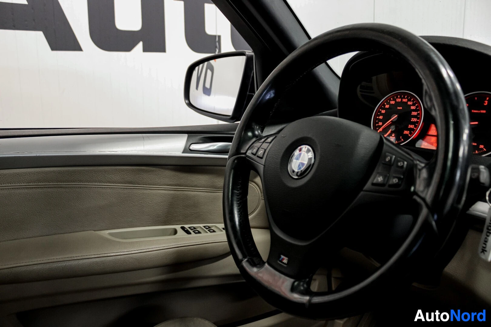 Ohjaamo: Ohjauspyörä, mittaristo ja oven sisäpaneeli kuvattuna kuljettajan paikalta. Ohjauspyörässä on BMW-logo ja oven panelissa sähköikkunoiden katkaisijat.