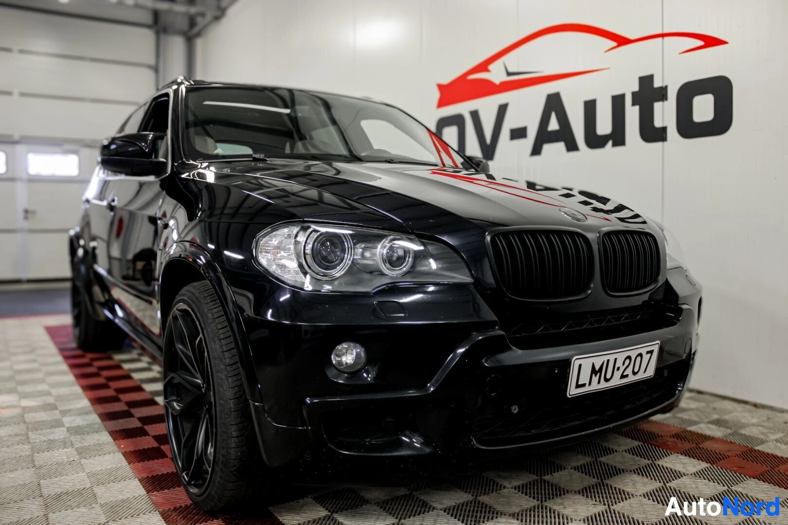 Etuviisto, nokka vasemmalle: Musta BMW X5 kuvattuna etuviistosta oikealta puolelta sisätiloissa. Autossa on mustat vanteet ja LED-ajovalot.