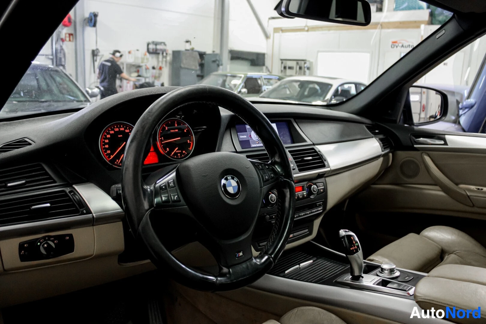 Ohjaamo: Kuvassa BMW:n ohjaamo, jossa nahkainen ohjauspyörä ja mittaristo punaisella valaistuksella. Kojelaudalla on keskinäyttö ja vaihteenvalitsin on keskikonsolissa.