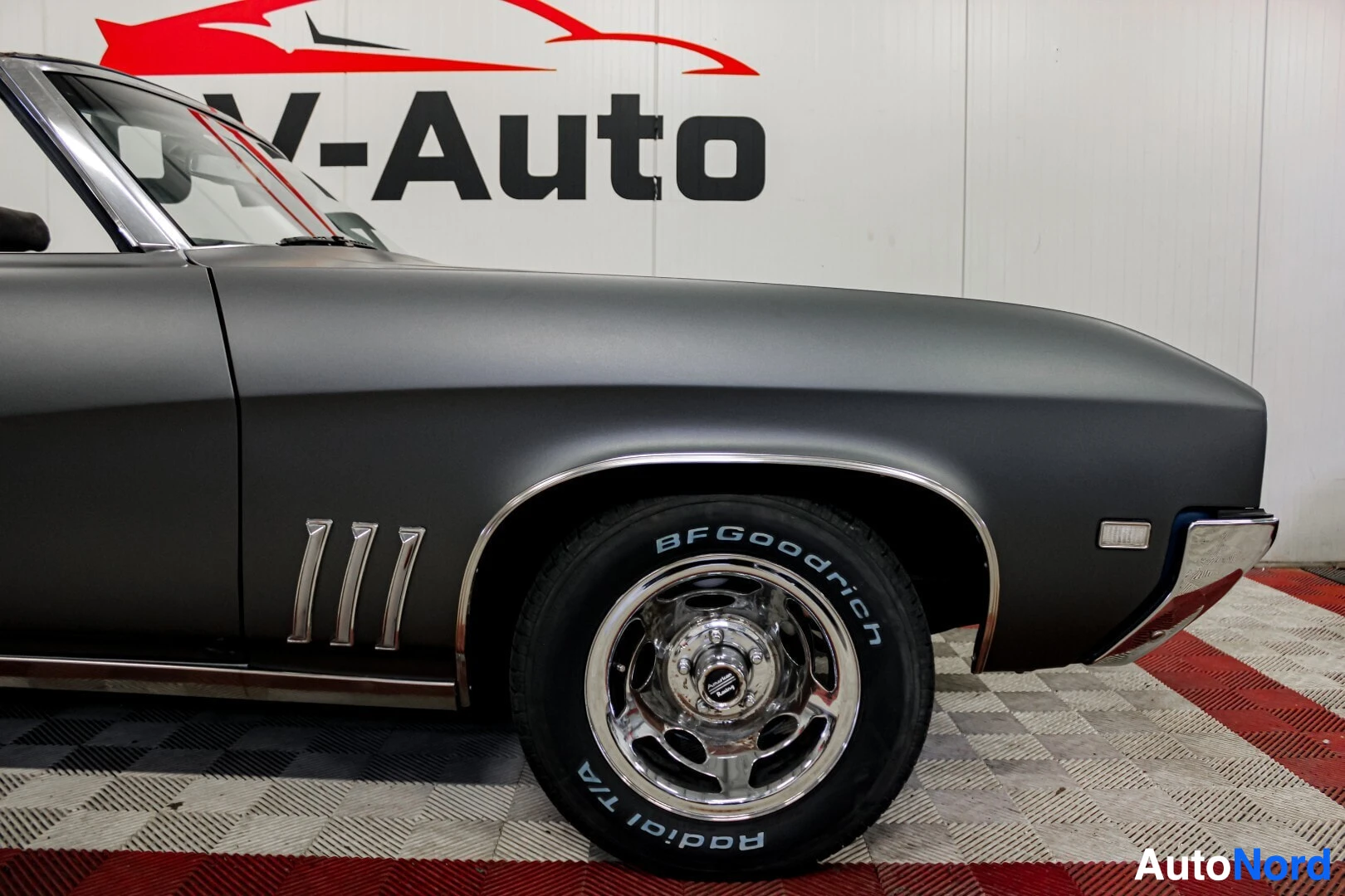 Yksityiskohta: Lähikuva auton eturenkaasta ja lokasuojasta, jossa on "BFGoodrich Radial T/A" -renkaan merkinnät ja kolme kromattua koristeuraa lokasuojassa.