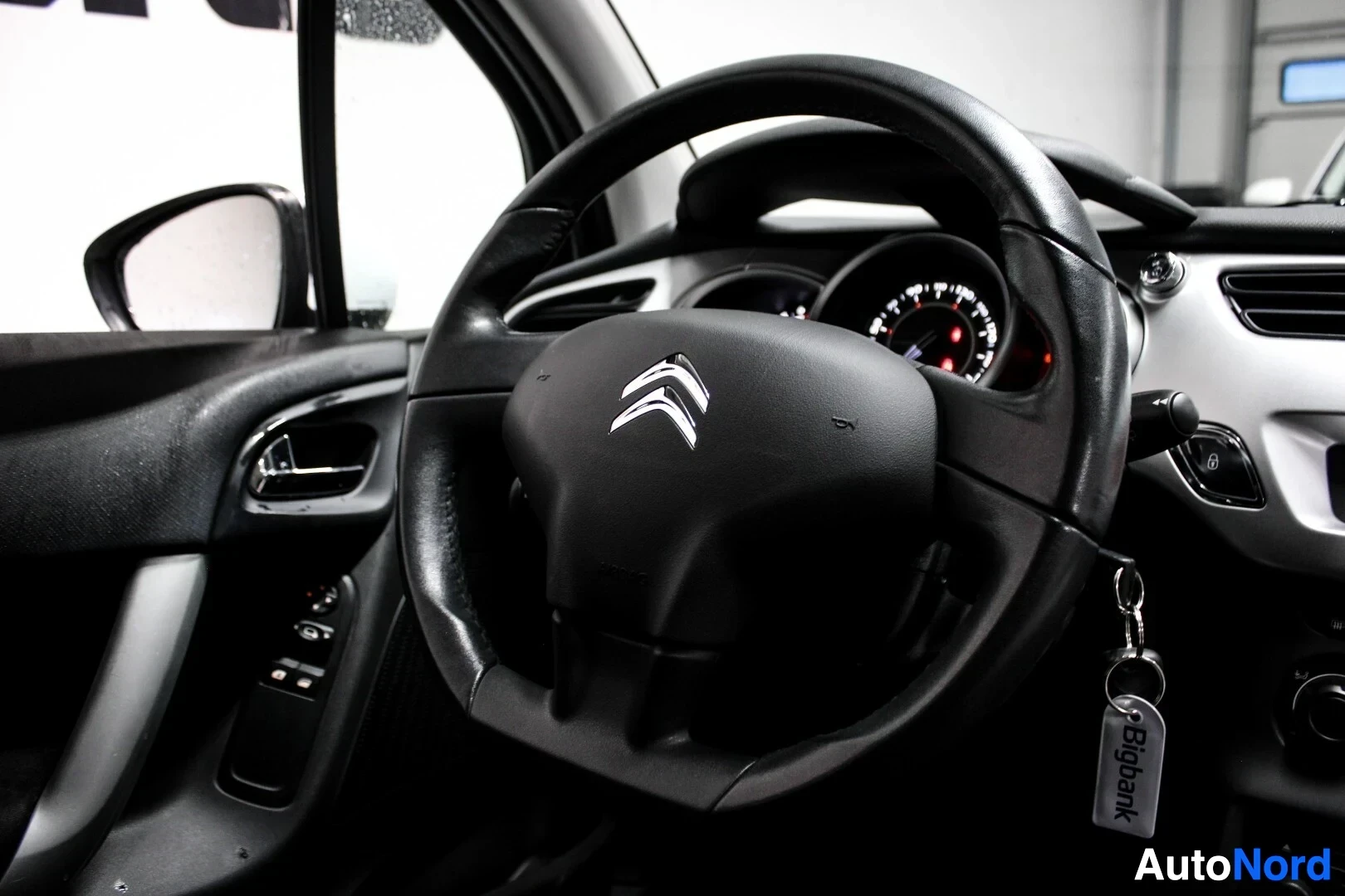 Ohjaamo: Ohjaamonäkymä, jossa näkyy ohjauspyörä Citroënin logolla ja auton avainnipussa Bigbank-avaimenperä.