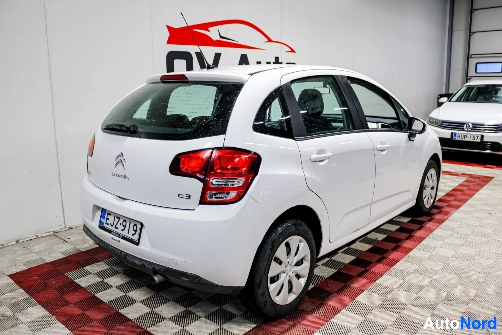 Takaviisto: Valkoinen Citroen C3 takaviistosta oikealta kuvattuna, pysäköitynä halliin. Auton rekisterinumero on