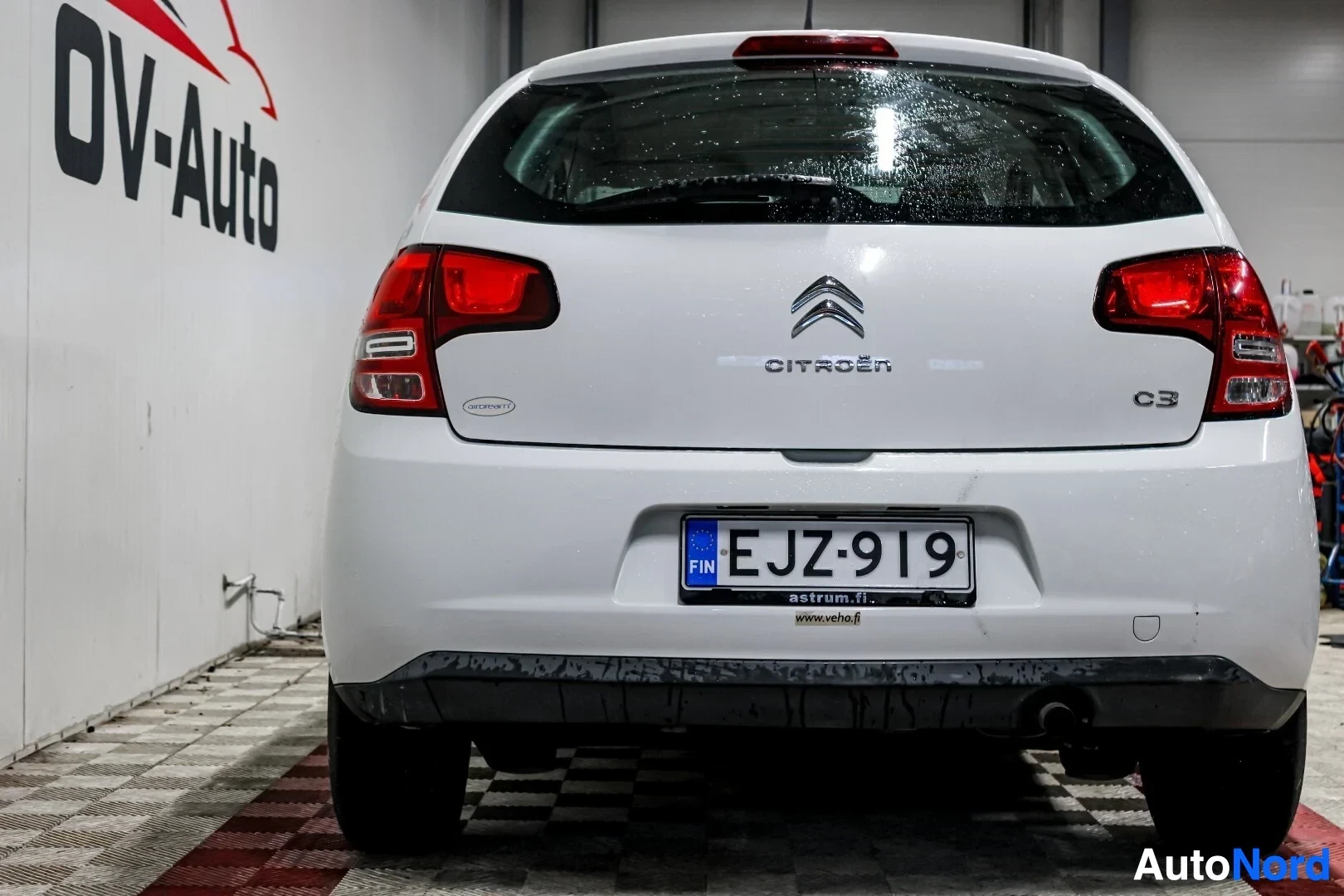 Takaa: Valkoinen Citroen C3 takaa päin kuvattuna, pysäköitynä halliin. Rekisterinumero on