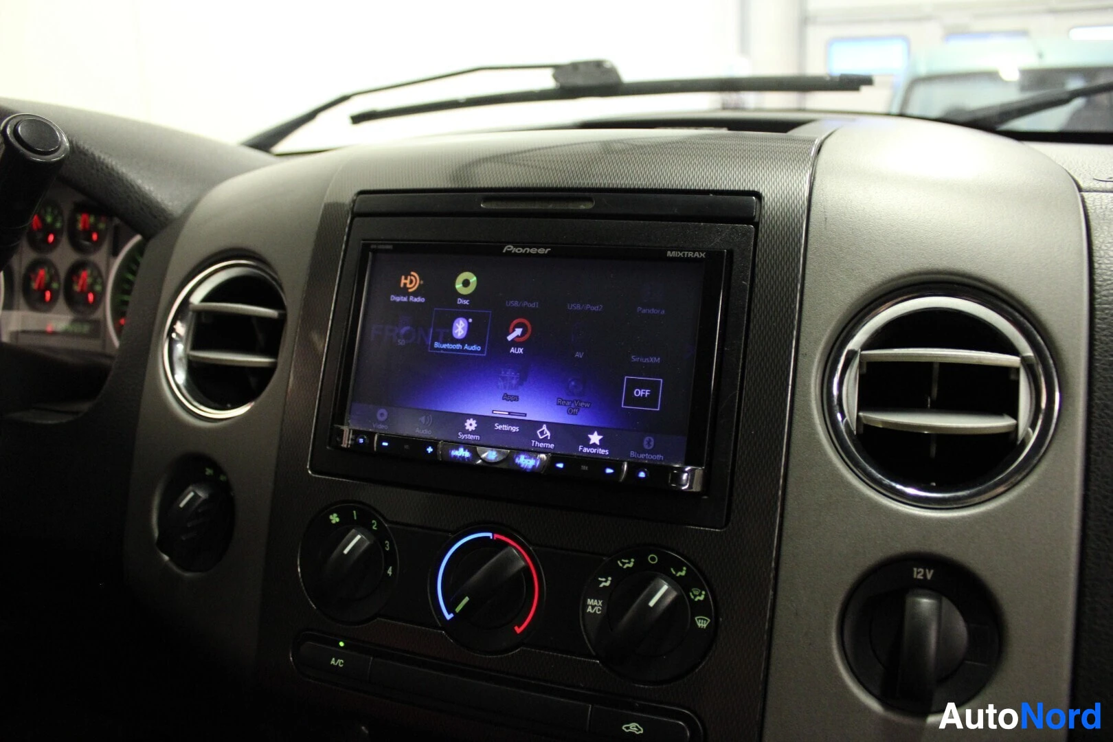 Yksityiskohta: Kojelaudan keskikonsoli, jossa on Pioneer-multimediasoitin. Näytöllä on useita kuvakkeita, kuten "Digital Radio", "Bluetooth Audio", "USB/iPod", "AUX" ja "Siriu