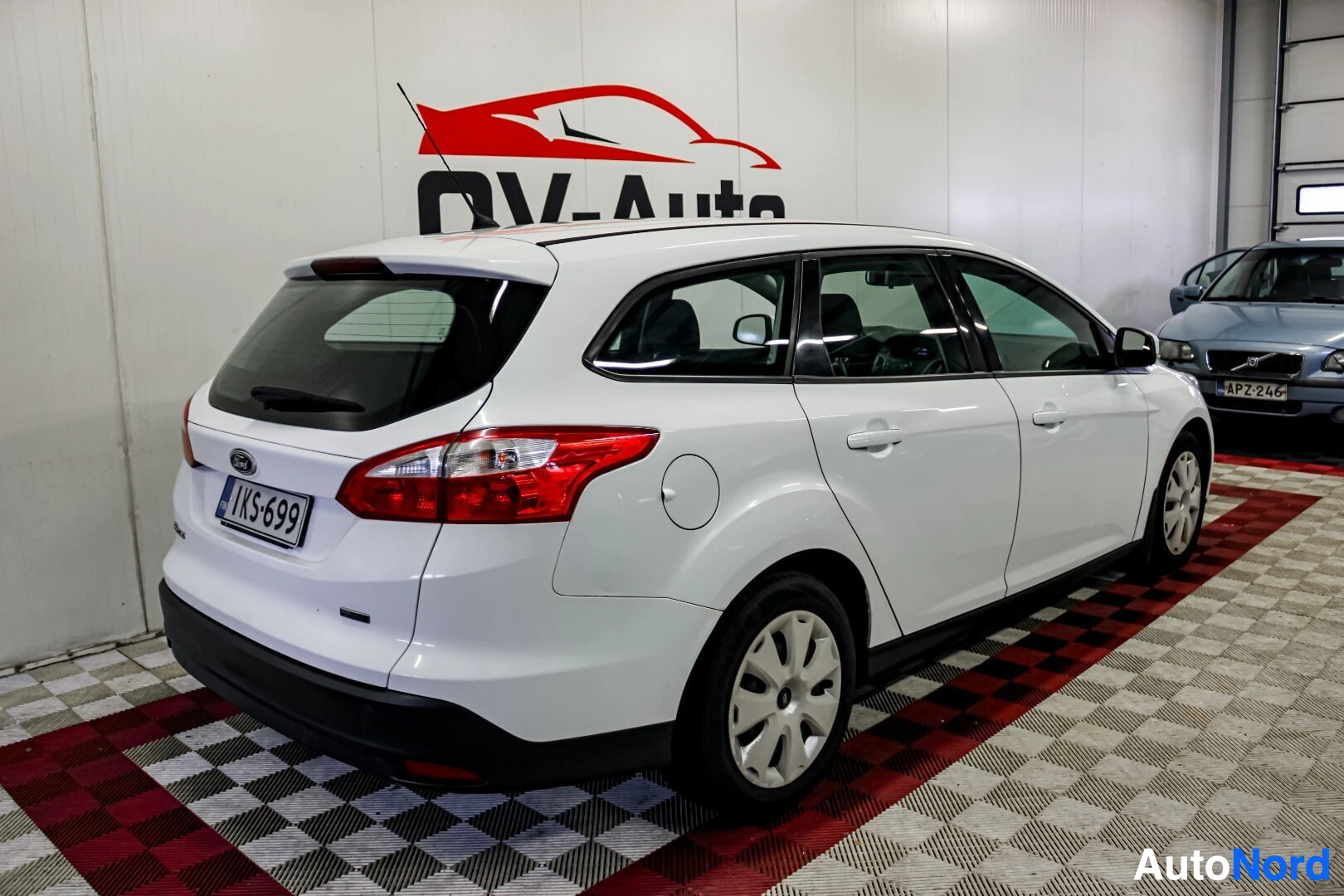 Takaviisto: Valkoinen farmariauto, Ford Focus, kuvattuna takavasemmalta. Autossa näkyvät takavalo ja sivupeili. Rekisterikilpi on asennettu perään