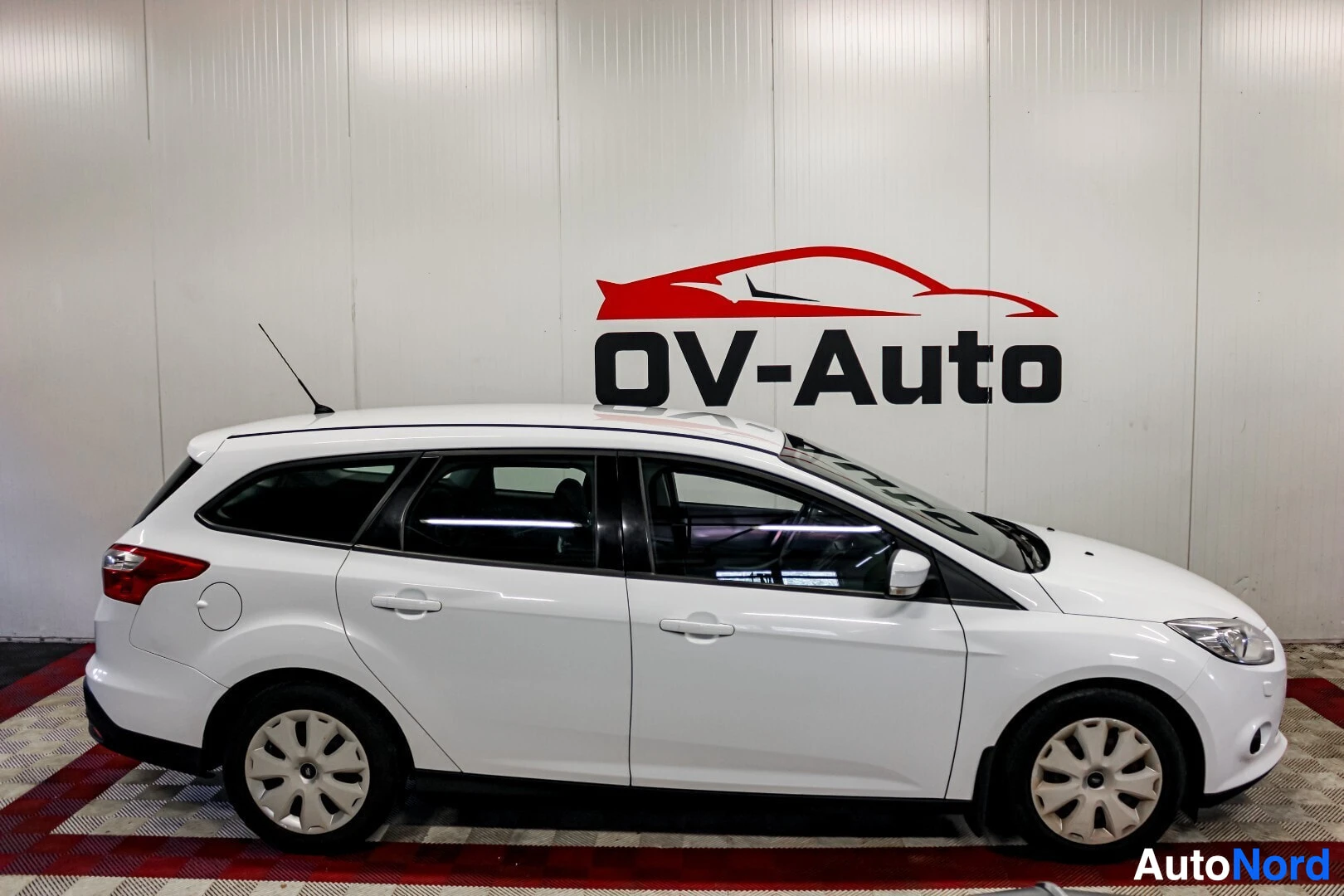 Sivulta: Valkoinen Ford Focus -farmariauto kuvattuna sivulta. Autossa on kattokaiteet ja alumiinivanteet.