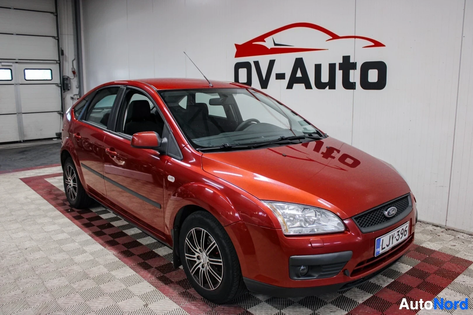 Etuviisto, nokka vasemmalle: Oranssinruskean Ford Focus -henkilöauton etuvasen kolmiulotteinen näkymä sisätilassa. Auton keula on käännetty vasemmalle. Autossa on musta etusäleikkö