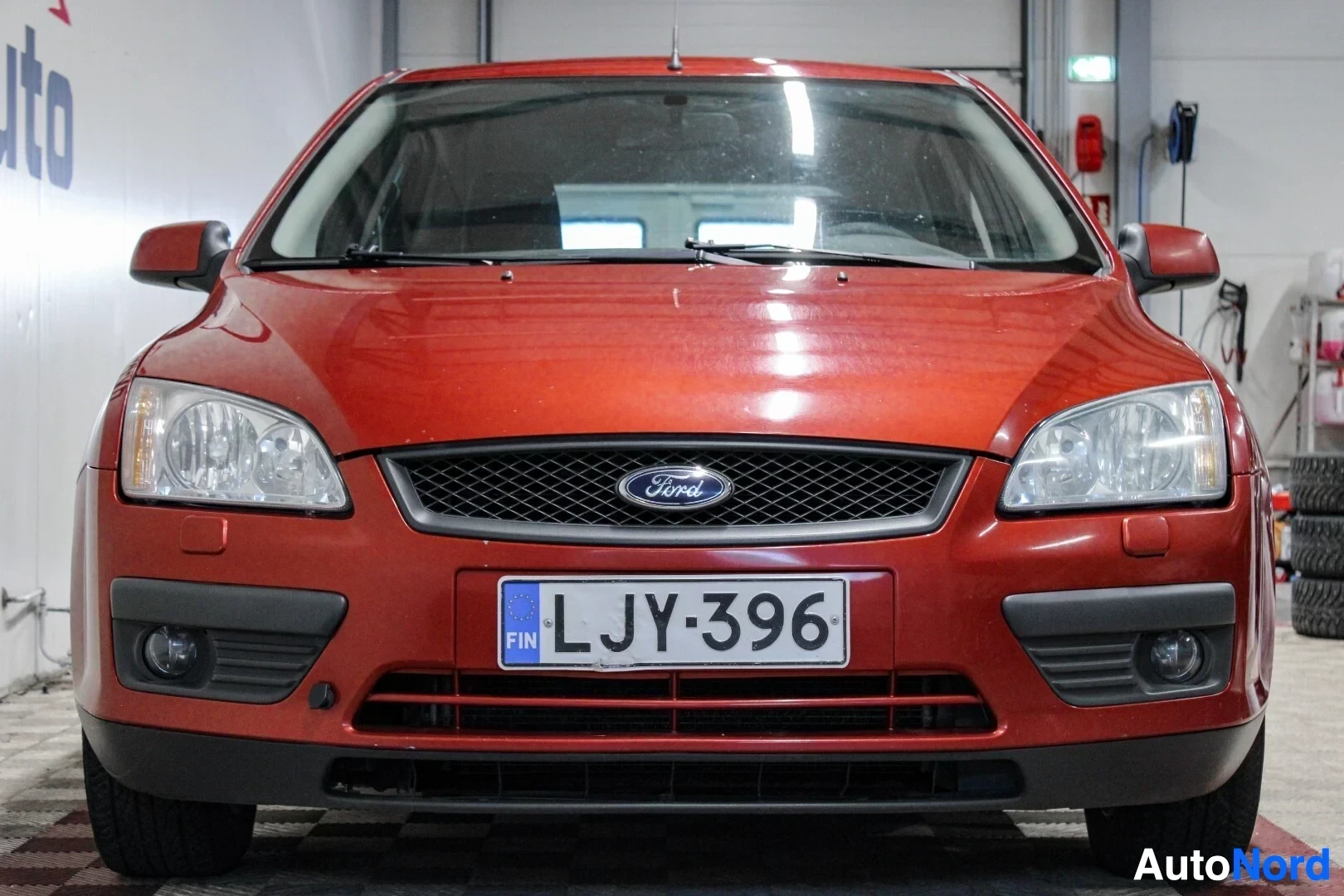 Edestä: Oranssinruskea Ford Focus -henkilöauton etuosa suoraan edestäpäin. Siinä on musta etusäleikkö, Ford-logo, sumuvalot ja valkoiset ajovalot. Rekisterikilpi