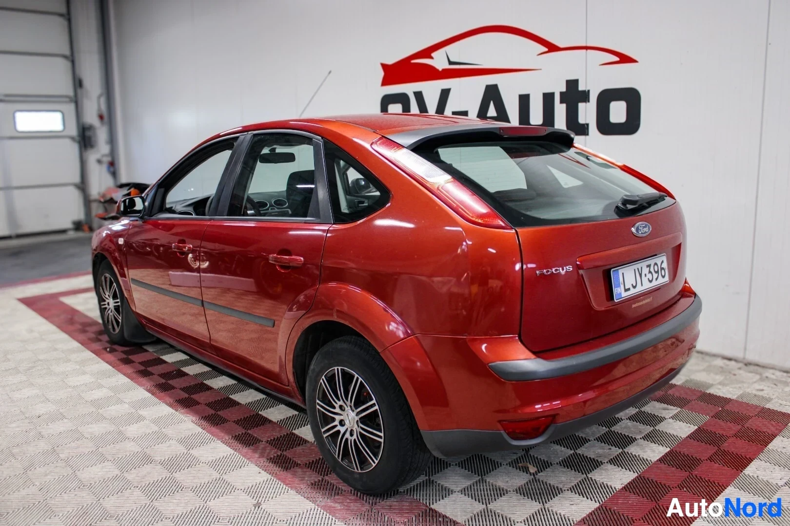 Takaviisto: Oranssinruskean Ford Focus -henkilöauton taka-oikea kolmiulotteinen näkymä sisätilassa. Takaluukussa on spoilerilippa ja 'FOCUS'-merkintä. Autossa on tummat tak