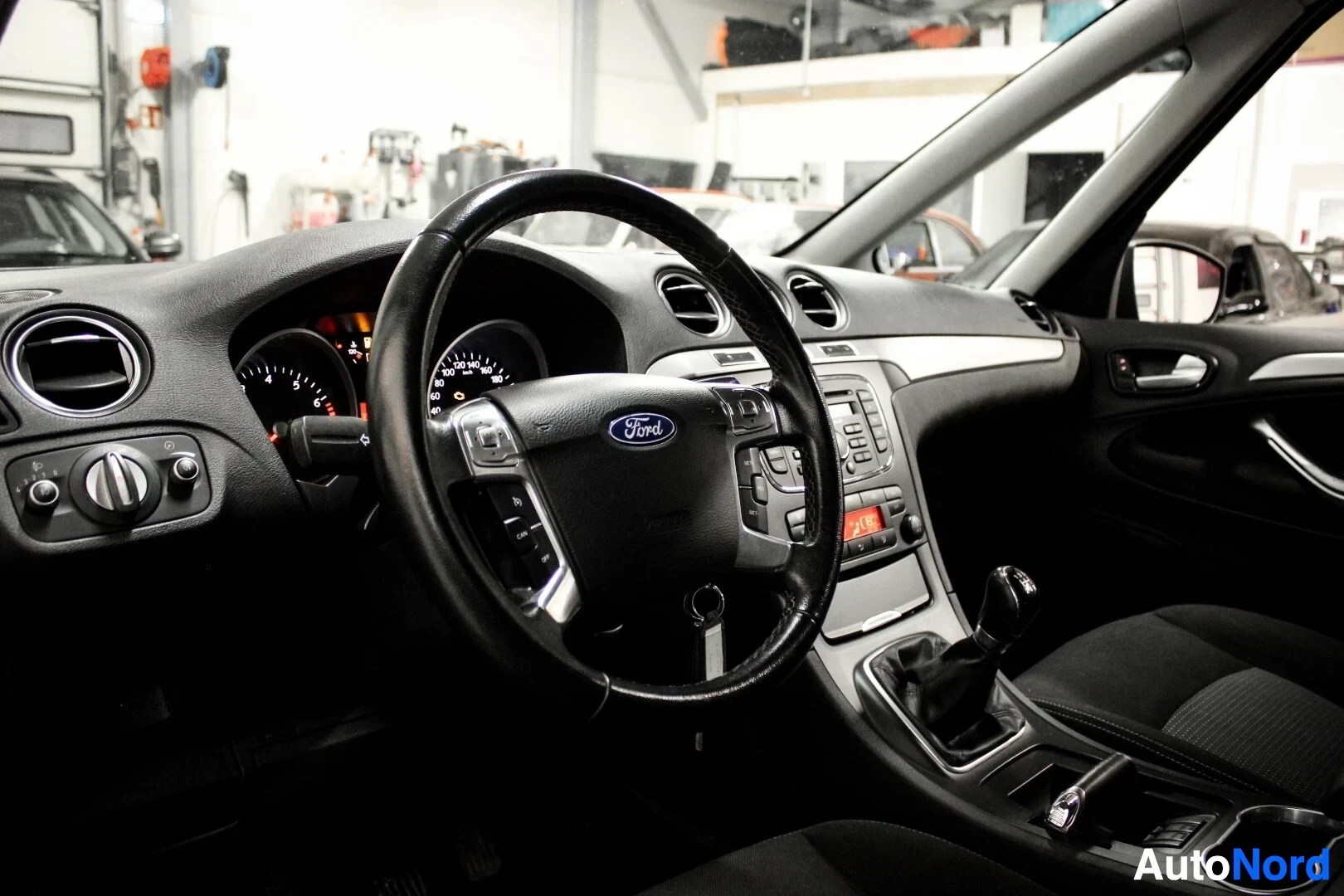 Ohjaamo: Kojelauta ja ohjauspyörä, jossa on Ford-logo ja ohjauspyörän painikkeet. Näkyvissä on myös manuaalivaihteiston valitsin ja ilmanvaihtoaukot.