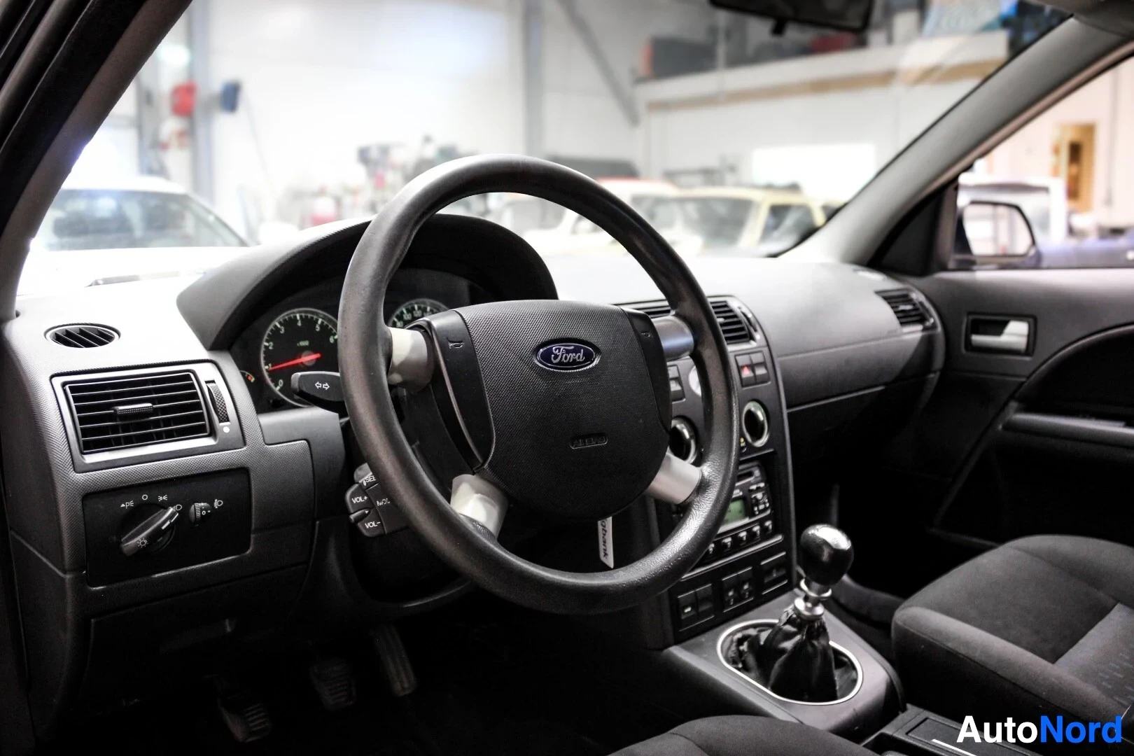 Ohjaamo: Sisäkuva, jossa näkyy ohjauspyörä, mittaristo ja kojelaudan keskialue. Ohjauspyörässä on "Ford"-logo.