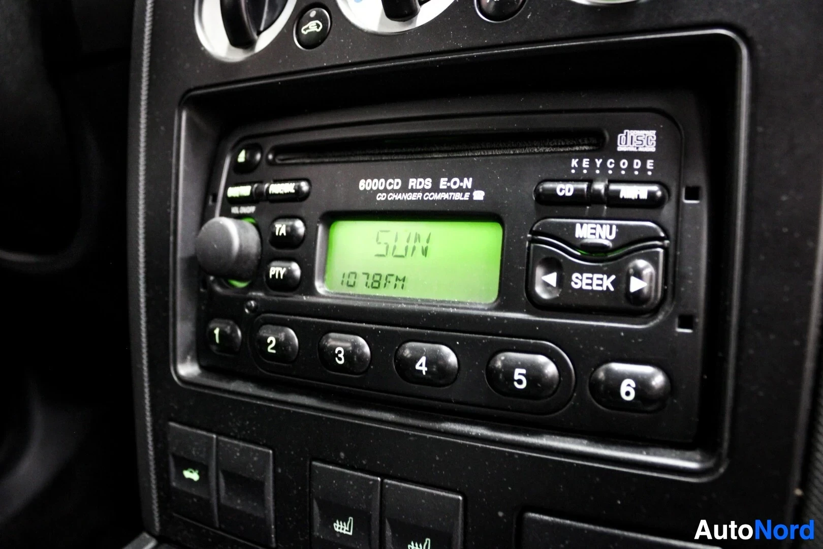 Yksityiskohta: Lähikuva auton 6000 CD RDS E-O-N CD-vaihdin yhteensopivasta radiosta, jossa näkyy digitaalinen näyttö "SUN 107.8 FM".