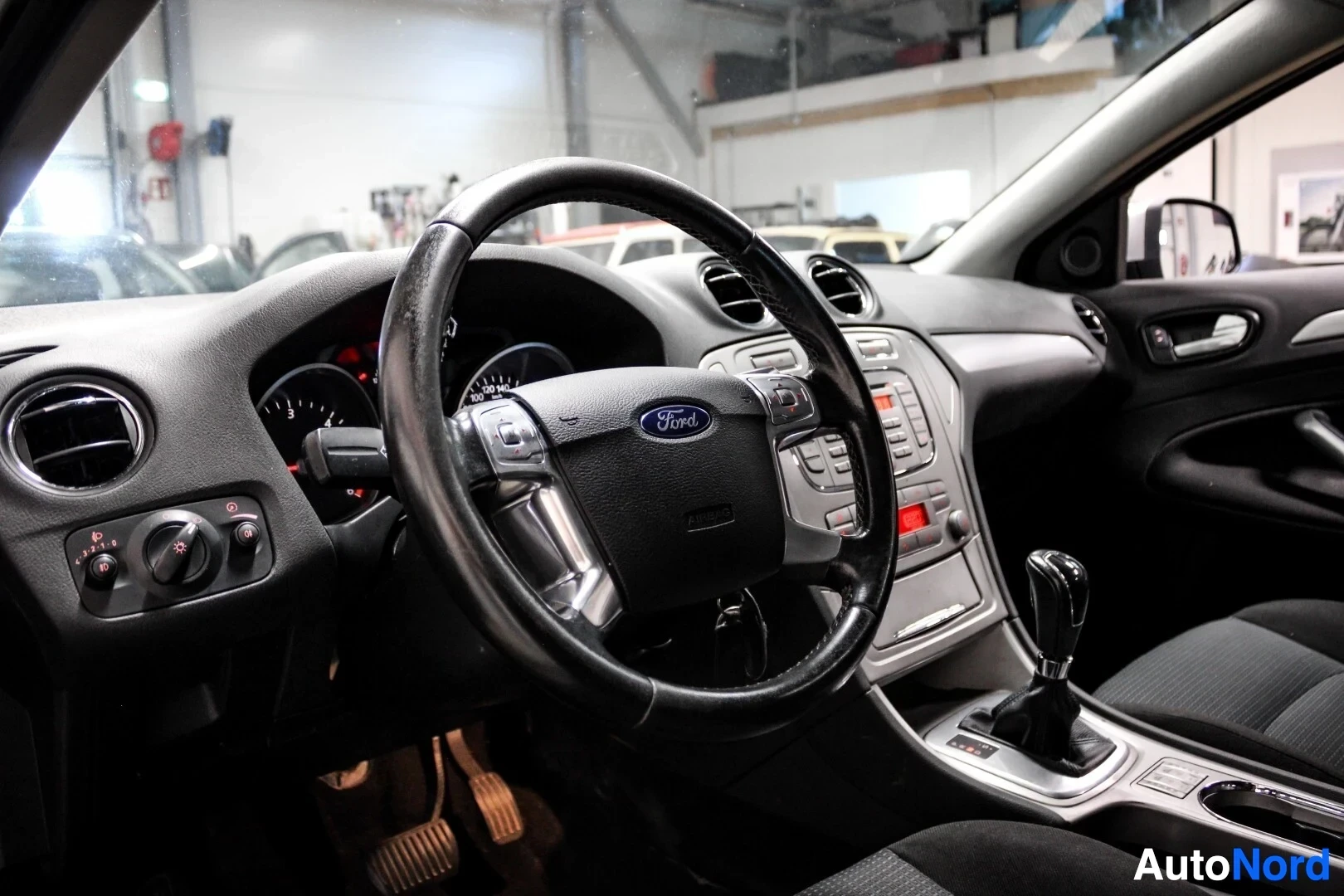 Ohjaamo: Kuvassa näkyy auton ohjaamo, etupenkiltä kuvattuna. Keskellä on monitoimiohjauspyörä, jossa on Ford-logo. Kojelaudassa näkyy ilmanvaihtosuuttimia, radio ja manu