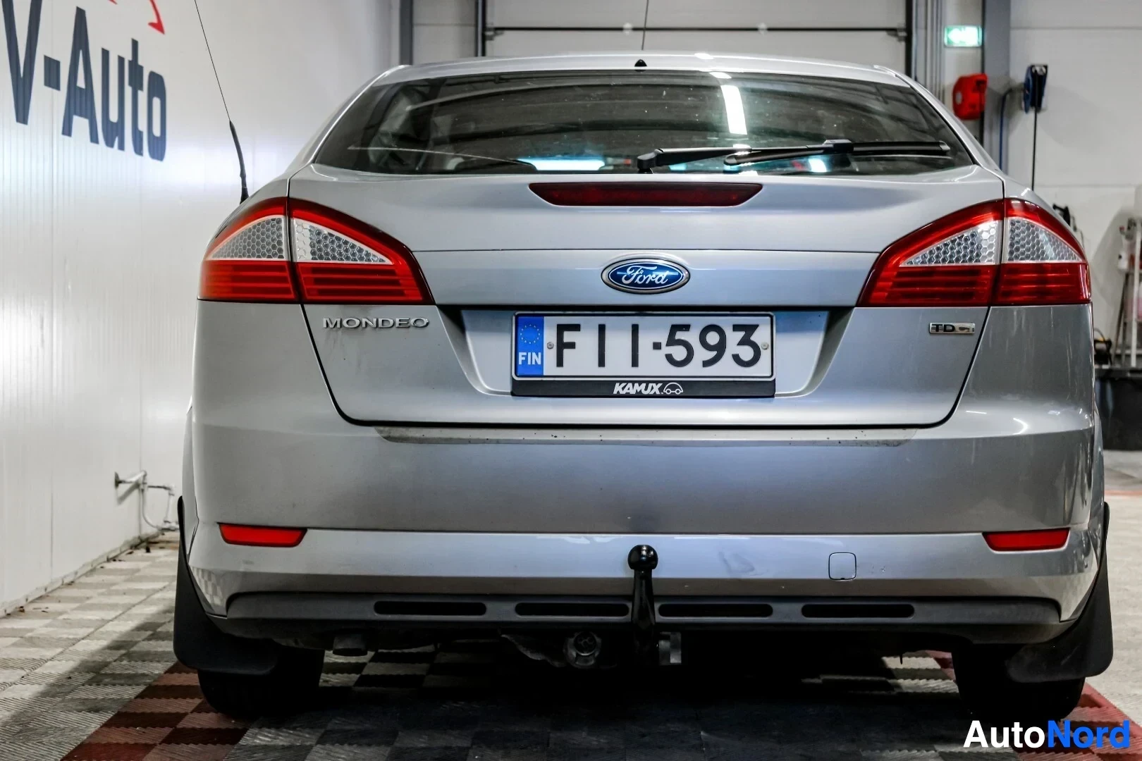 Takaa: Hopeanharmaan Ford Mondeon takaosa, rekisterikilpi "", vetokoukku näkyvissä. Auto on kuvattu takaa päin sisätiloissa