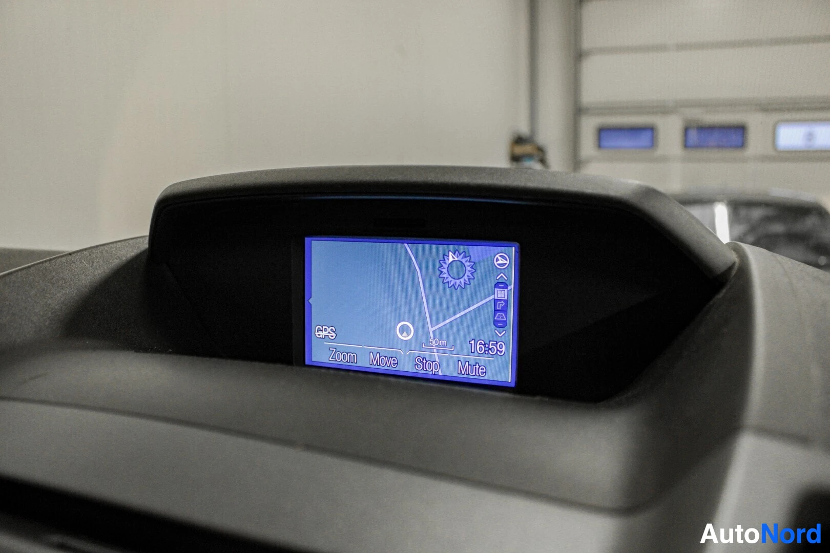 Yksityiskohta: Lähikuva kojelaudan päällä olevasta auton näytöstä, jossa näkyy GPS-kartta ja kellonaika 16:59.