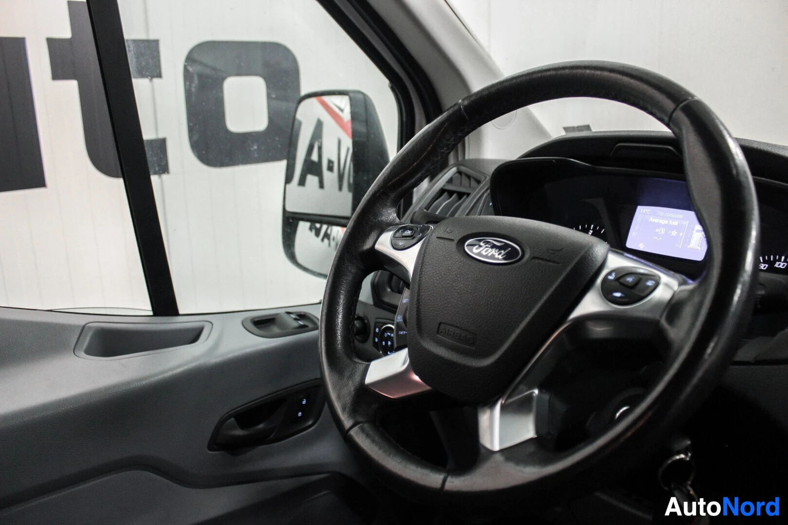 Yksityiskohta: Lähikuva ohjauspyörästä, jossa on Ford-logo ja monitoiminäppäimet. Kojelaudan näyttö näkyy taustalla.
