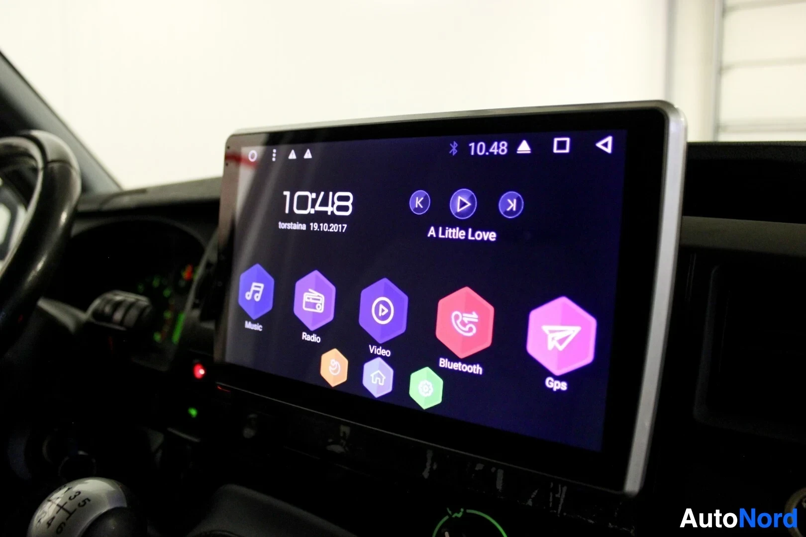 Yksityiskohta: Lähikuva kojelaudan suuresta kosketusnäytöstä, jossa näkyy musiikki-, radio-, video-, Bluetooth- ja GPS-kuvakkeet. Ruudulla on myös kellonaika 10:48 ja päivämää