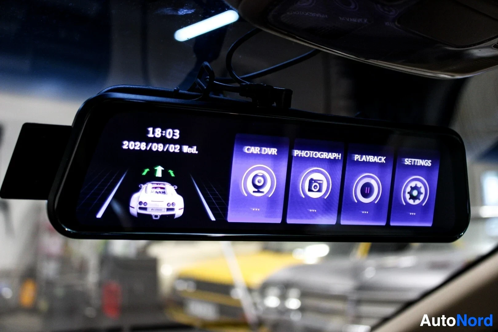 Yksityiskohta: Lähikuva taustapeiliin asennetusta näytöstä, joka näyttää käyttöliittymän valikot, kuten "CAR DVR", "PHOTOGRAPH", "PLAYBACK" ja "SETTINGS". Näytön vasemmassa re