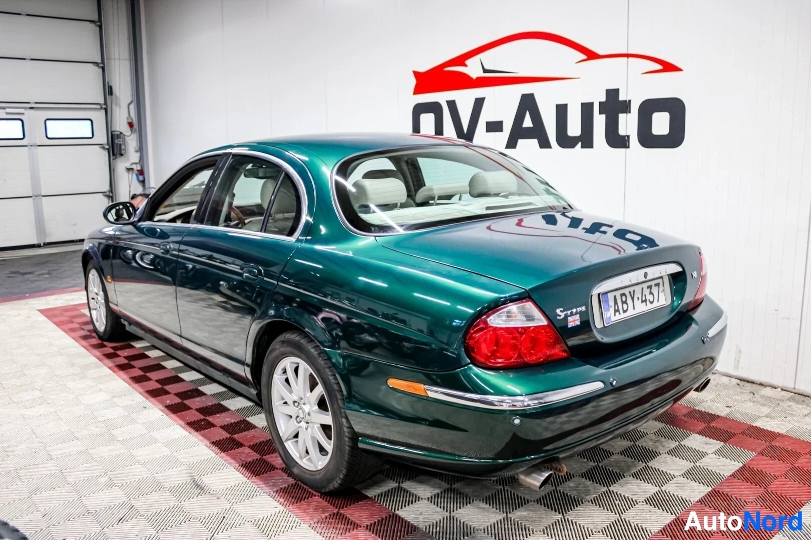 Takaviisto: Tummanvihreä henkilöauto, jonka takaosa ja oikea kylki ovat näkyvissä. Takaosassa on takavalot ja rekisterikilpi "S-Type ". Pakoputki näkyy auton oikeall