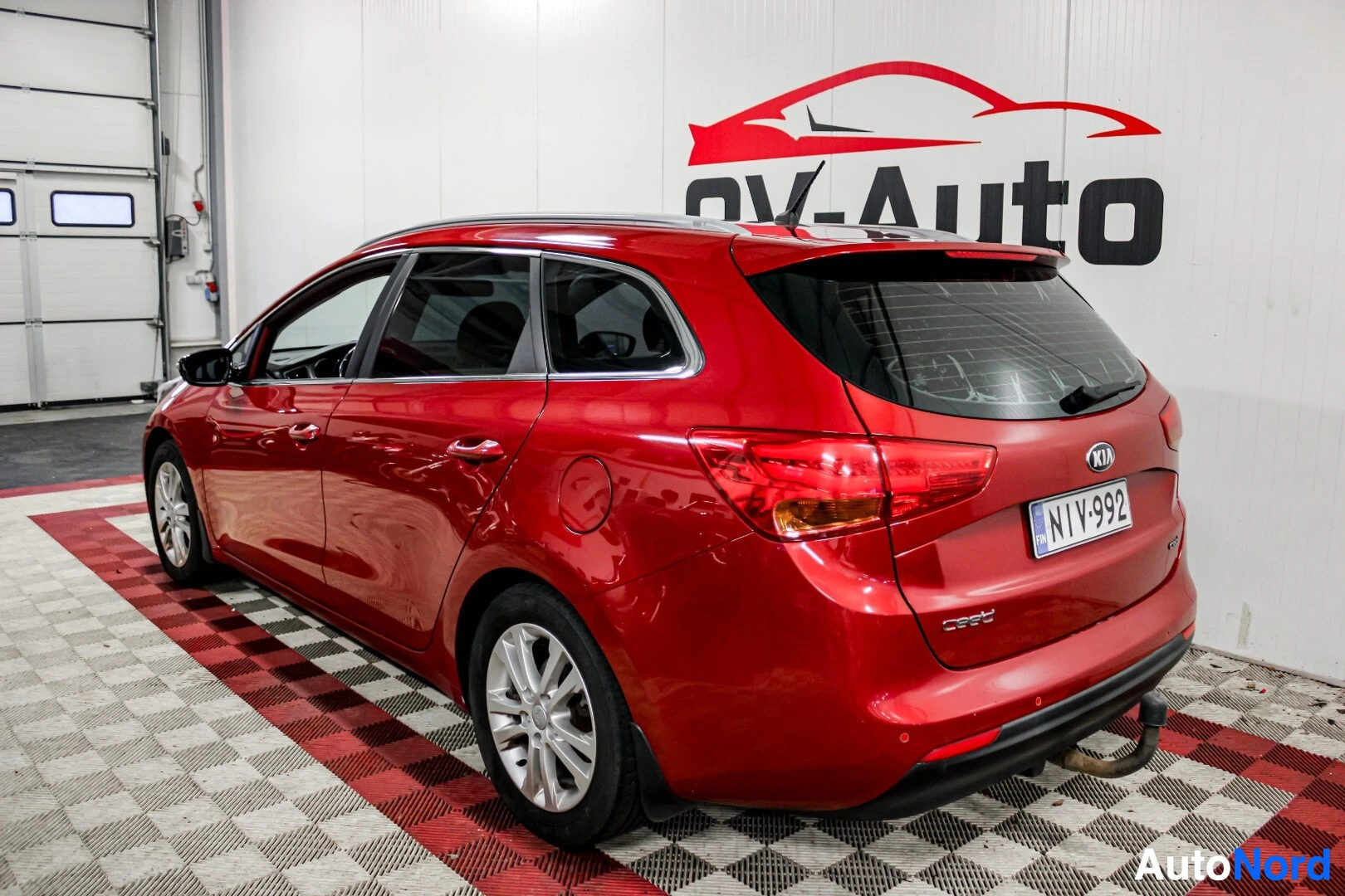 Takaviisto: Punainen Kia Ceed farmarimalli kuvattuna takaviistosta takaa päin katsoen oikealle. Autossa on kevytmetallivanteet, kattokiskot ja vetokoukku.
