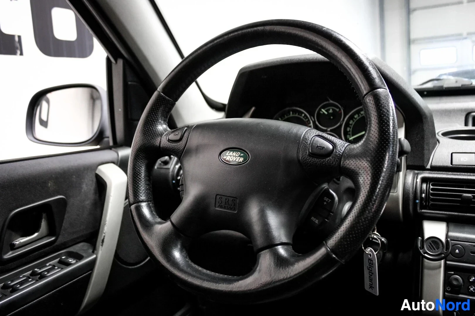 Yksityiskohta: Lähikuva ohjauspyörästä, jossa on "LAND ROVER" -logo ja "SRS AIRBAG" -merkintä. Avaimet roikkuvat virtalukossa.