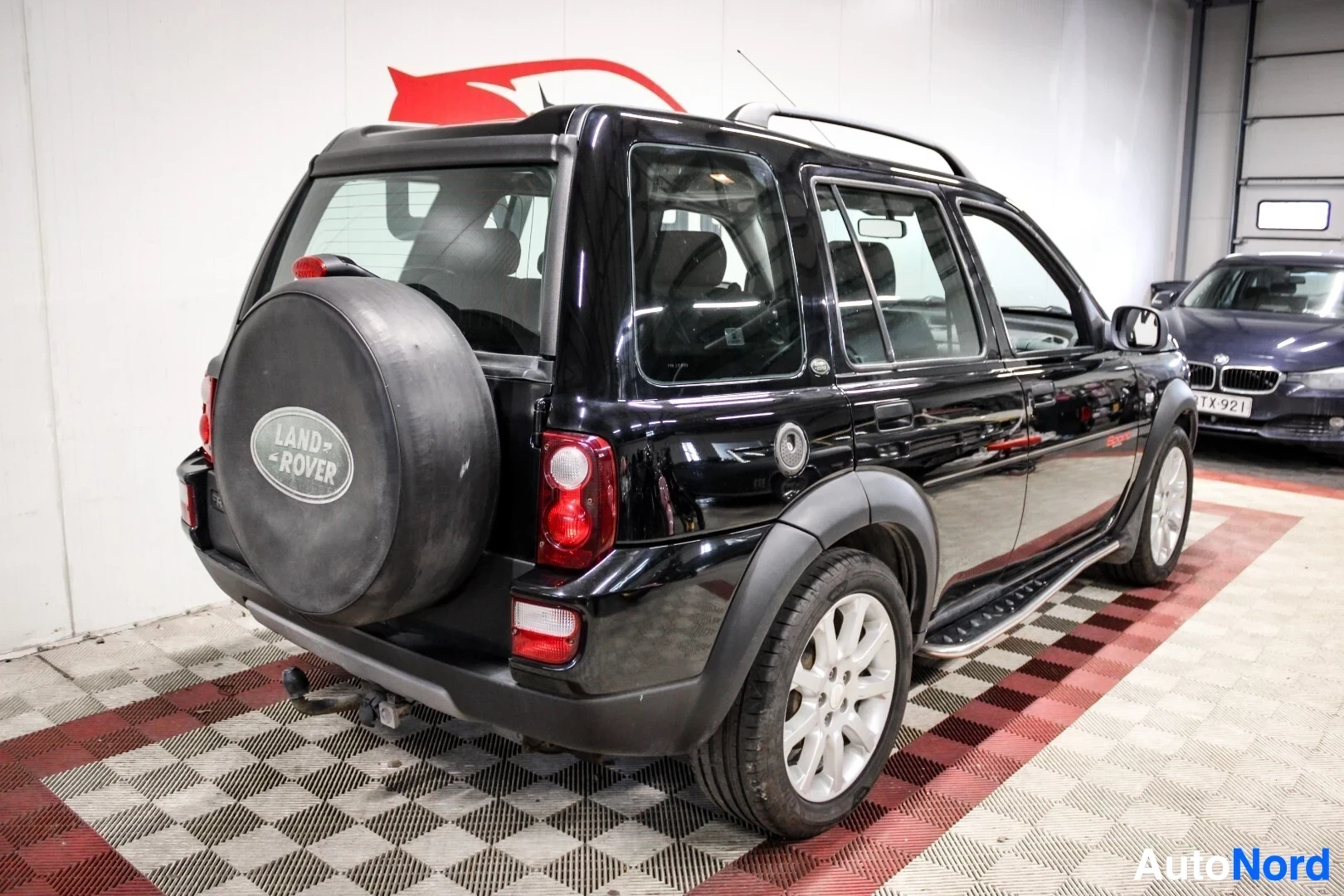 Takaviisto: Musta Land Rover Freelander pysäköitynä halliin. Ajoneuvon oikea kylki ja takaosa ovat näkyvissä. Takaluukussa on vararengas, jonka suojapeitteessä on Land Rove