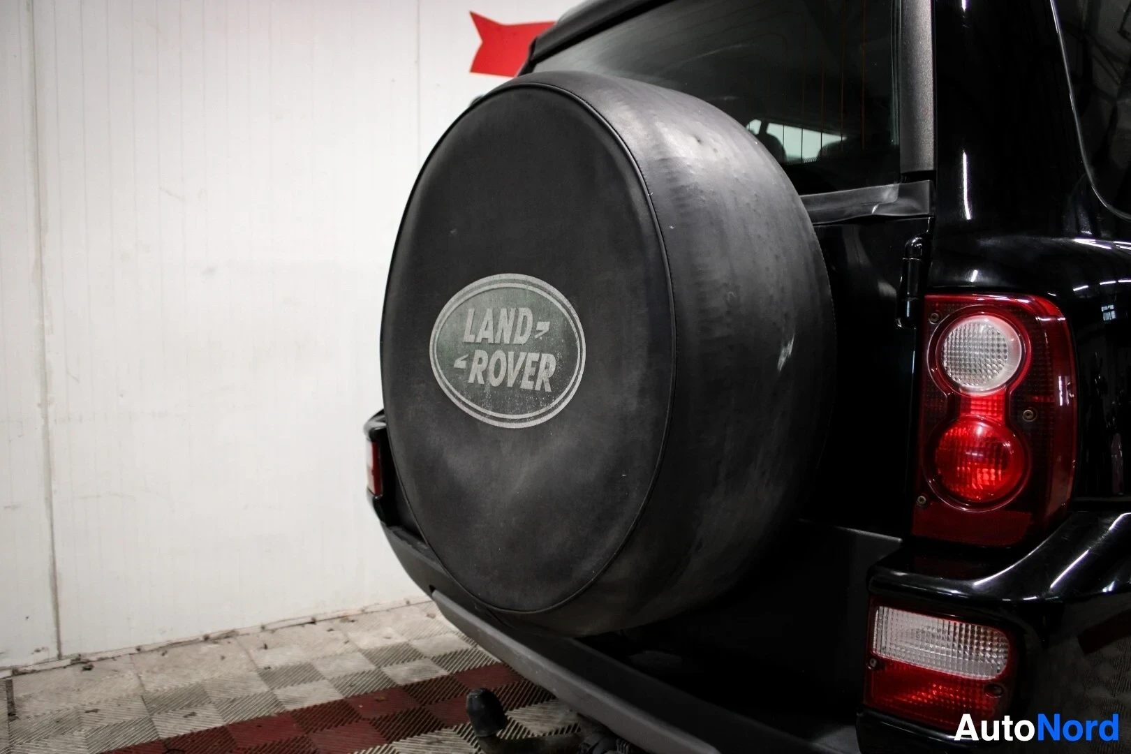 Yksityiskohta: Lähikuva mustasta vararenkaan suojapeitteestä takaluukussa. Peitteessä on Land Rover -logo ja tekstiä.