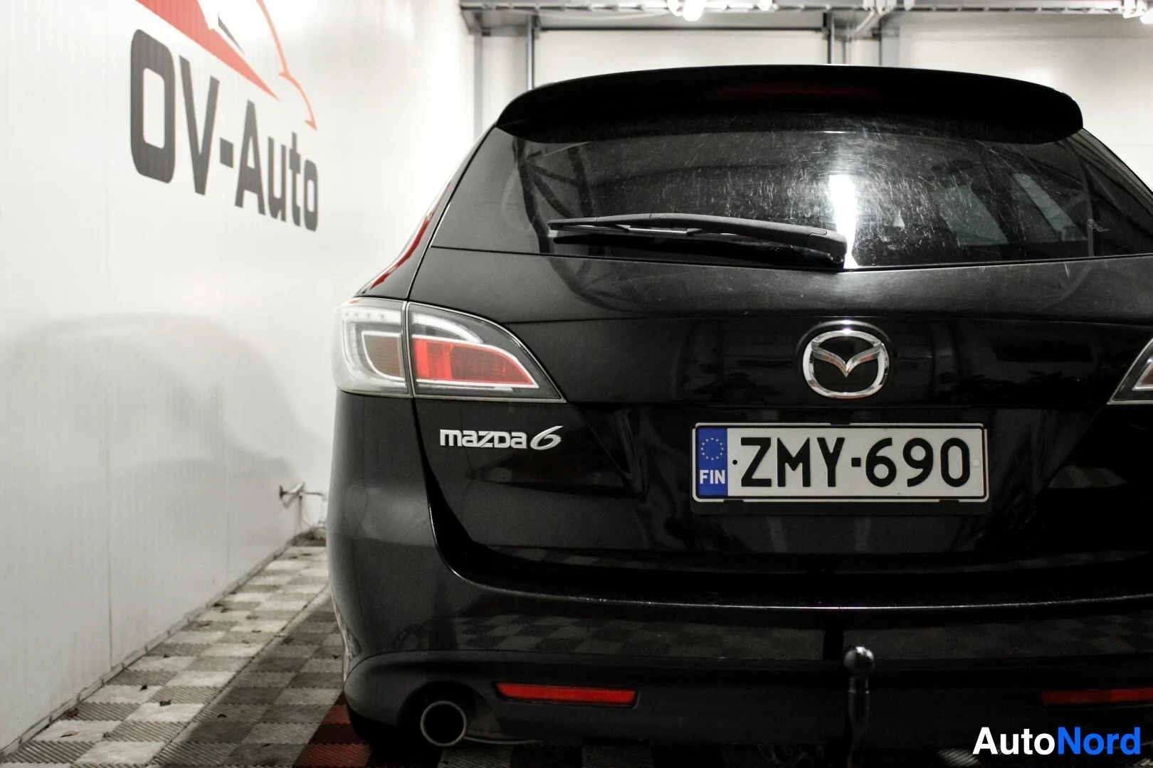 Takaa: Musta farmariauto, jonka takaosa näkyy, rekisterikilpi. Auton takaluukussa on Mazda-logo ja takavalot ovat näkyvissä. Kuvassa näkyy myös vetokoukku