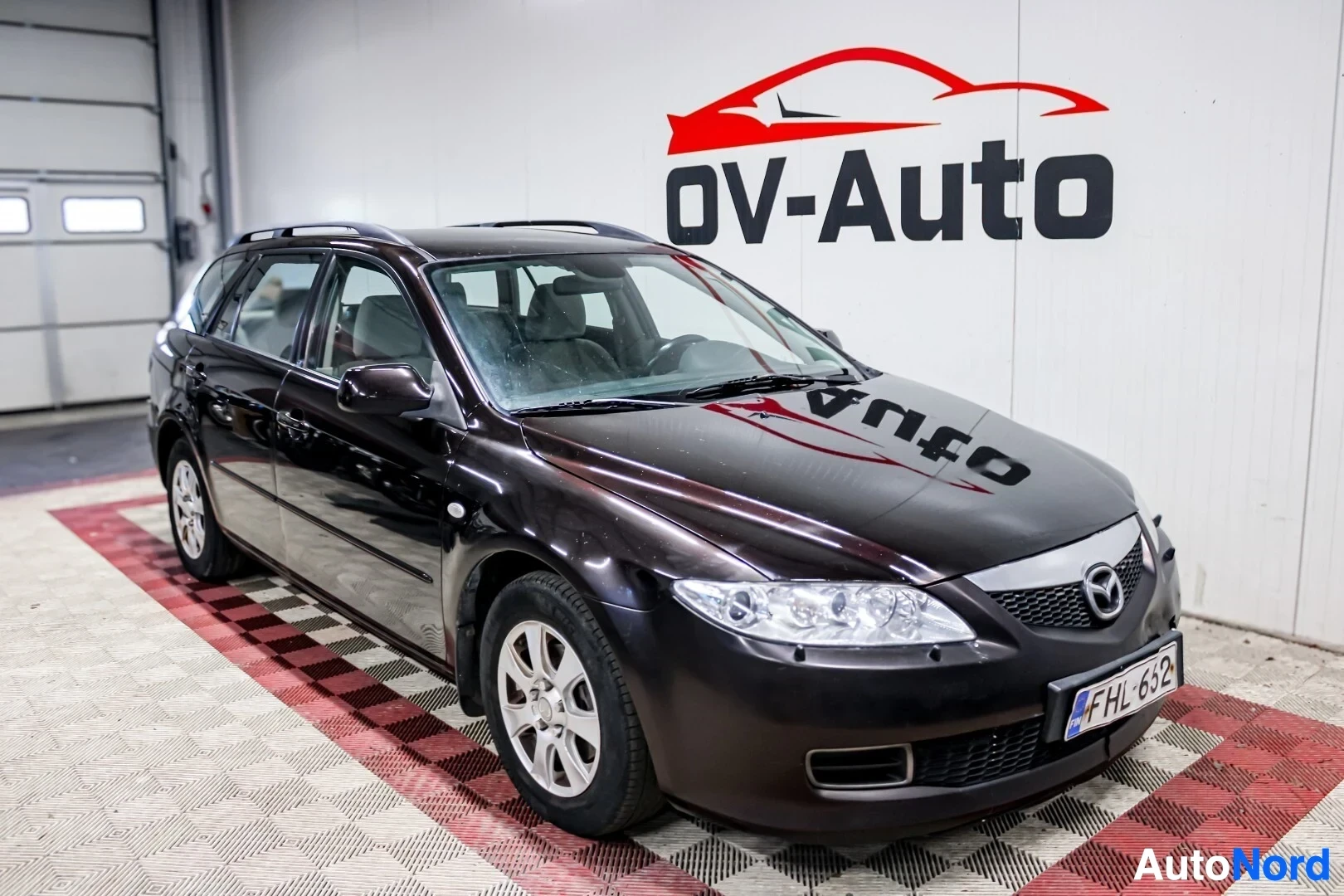 Etuviisto, nokka oikealle: Ruskea farmariauto edestä ja vasemmalta sivulta kuvattuna sisätiloissa, autossa on kattokaiteet ja kevytmetallivanteet. Rekisterikilpi on