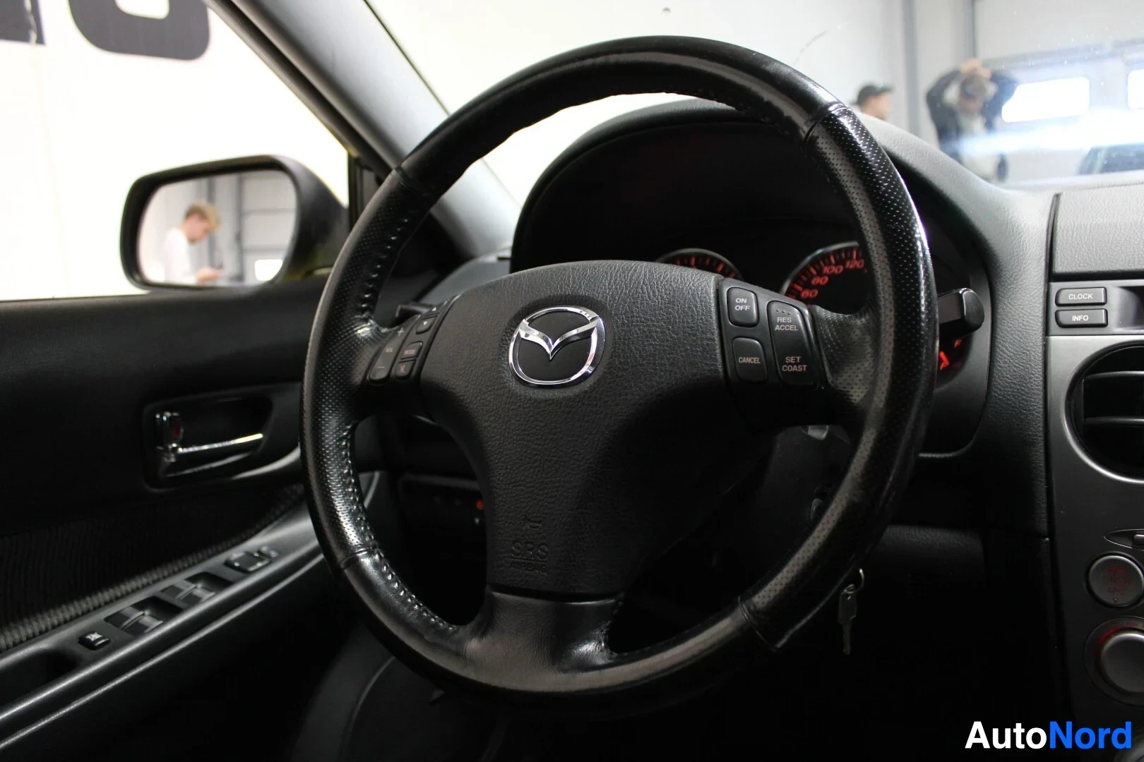 Yksityiskohta: Lähikuva ohjauspyörästä, jossa on Mazda-logo ja ohjauspyörän painikkeita.