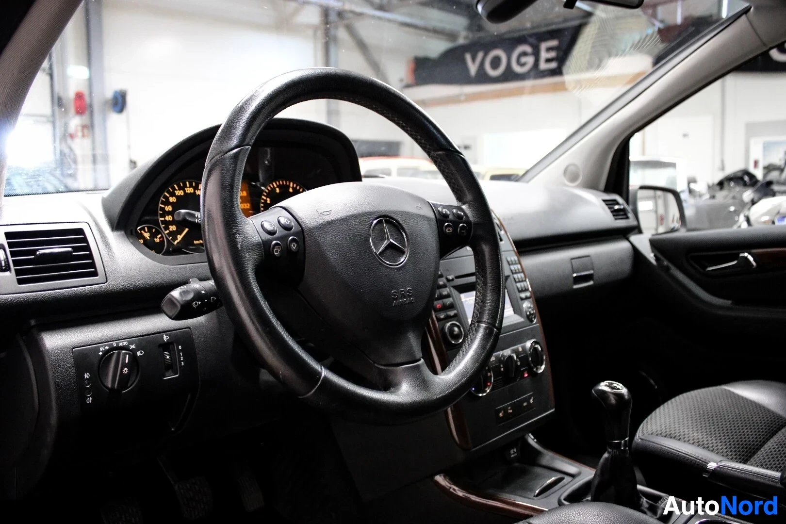 Ohjaamo: Ohjauspyörä, jossa on Mercedes-Benzin logo ja monitoiminäppäimet. Taustalla näkyy mittaristo ja osittain keskikonsoli.