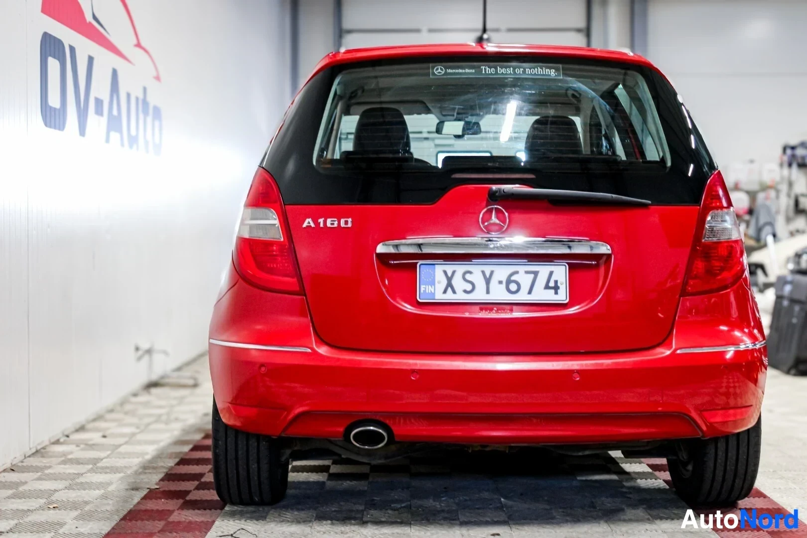 Takaa: Punainen henkilöauto takaa, rekisterikilpi. Takalasin yläreunassa lukee "Mercedes-Benz The best or nothing."