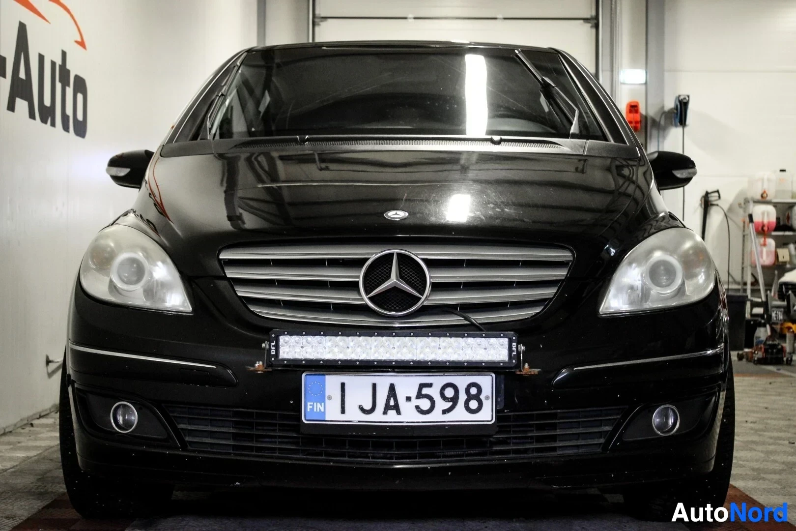Edestä: Mustan henkilöauton etuosa kuvattuna suoraan edestä. Auton keskellä on Mercedes-Benz-logo ja maski, alla on lisävalopaneeli ja rekisterikilpi