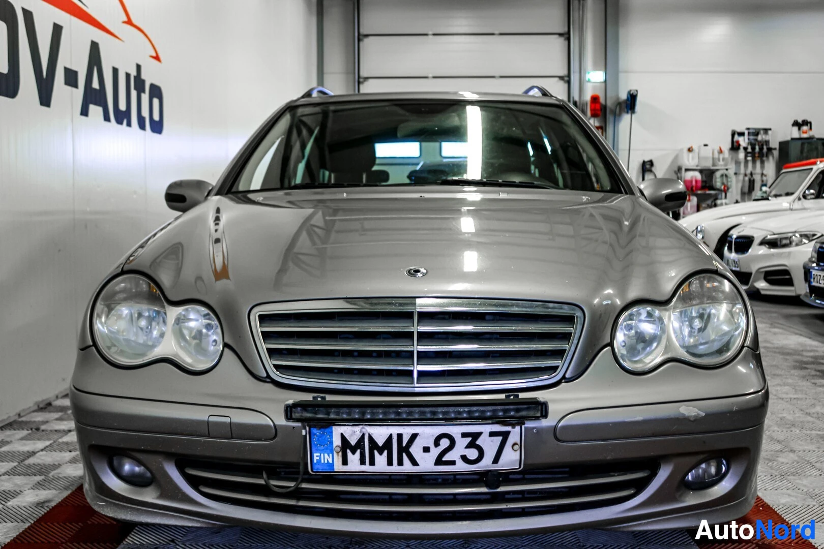 Edestä: Harmaa farmariauto edestä päin kuvattuna. Auton etupuskurissa on rekisterikilpi ja lisävalopaneeli.