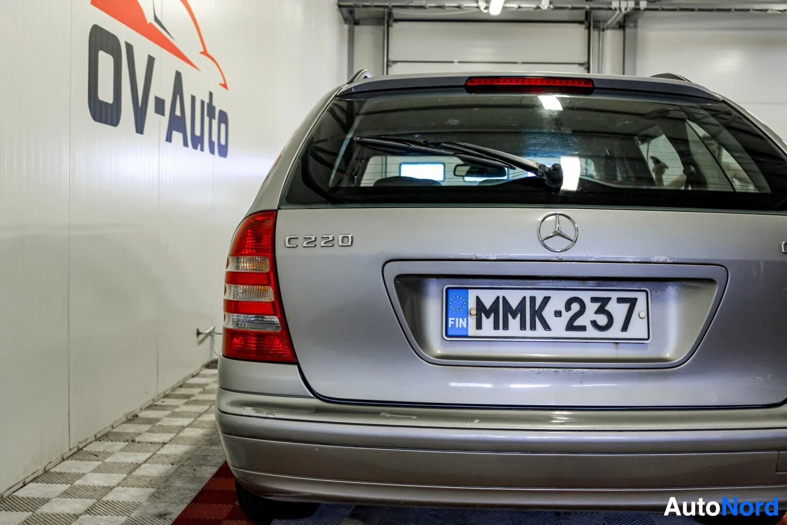 Takaa: Harmaan Mercedes-Benz C-sarjan farmariauton takaosa, jossa rekisterikilpi, vasen takavalo ja takaluukussa C220-merkintä. Takalasinpyyhin on yläasennossa