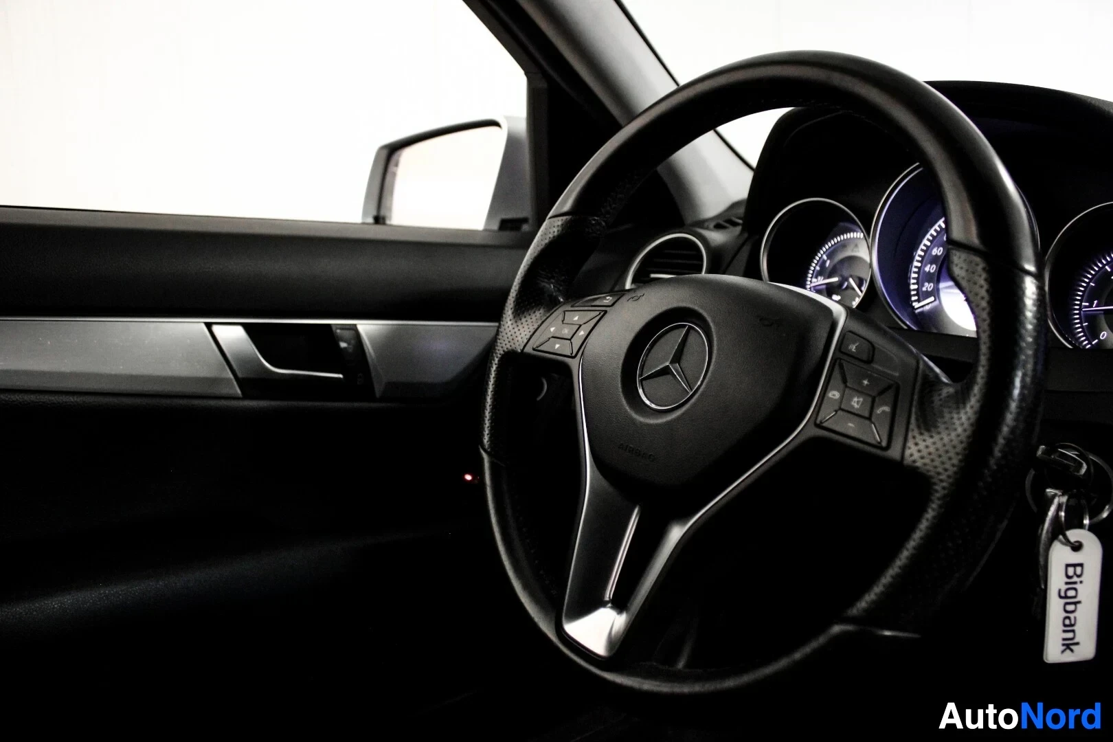 Yksityiskohta: Musta nahkainen monitoimiohjauspyörä kolmella puolalla. Ohjauspyörän keskellä on Mercedes-Benz-logo. Ohjauspyörän oikealla puolella on säätöpainikkeita. Virta-a