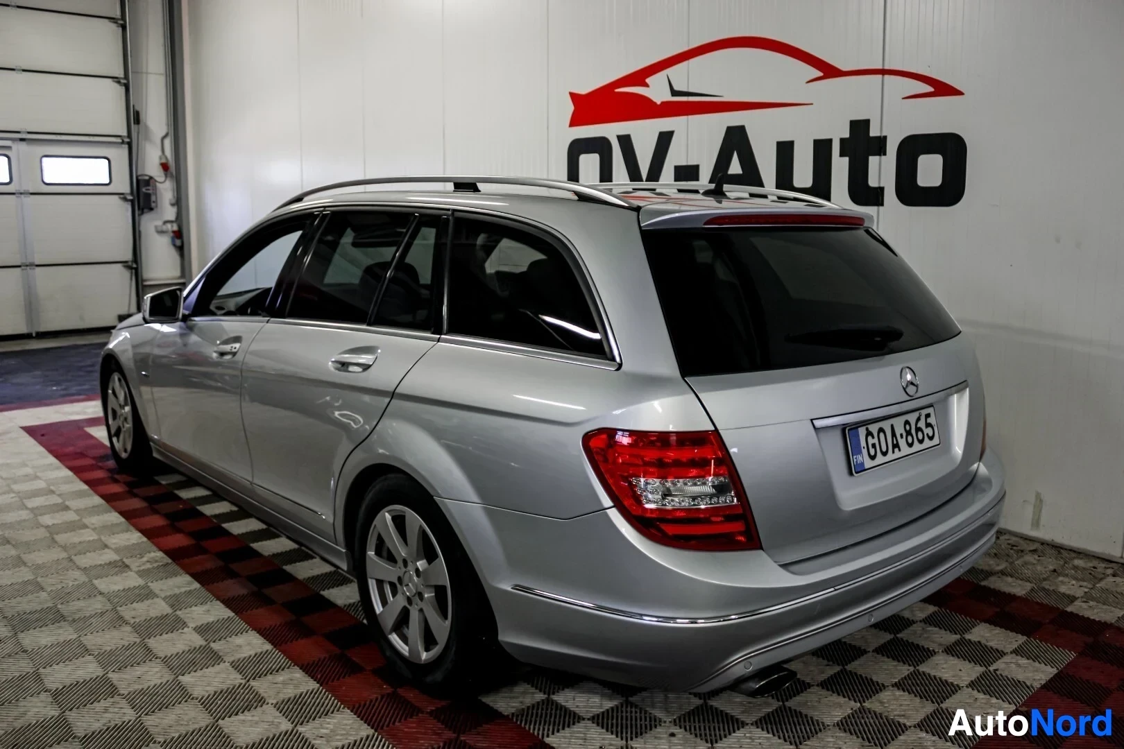 Takaviisto: Hopeanvärinen Mercedes-Benz C-sarjan farmari, jossa on kattokaiteet, takana Suomen rekisterikilpi ja viisispakkaiset kevytmetallivanteet. Auto on pysäkö