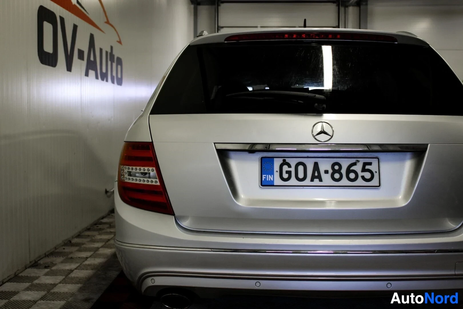 Takaa: Lähikuva Mercedes-Benz C-sarjan farmariauton perästä, jossa on Suomen rekisterikilpi, peräkontin keskellä tähtilogo ja takapuskurissa pysäköintianturit