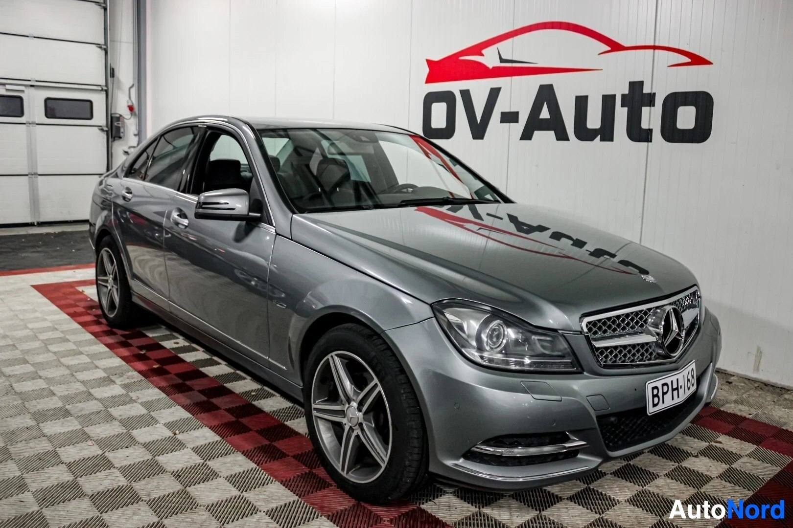 Etuviisto, nokka oikealle: Harmaa Mercedes-Benz C-sarjan sedan etuviistosta oikealta, rekisterikilpi.