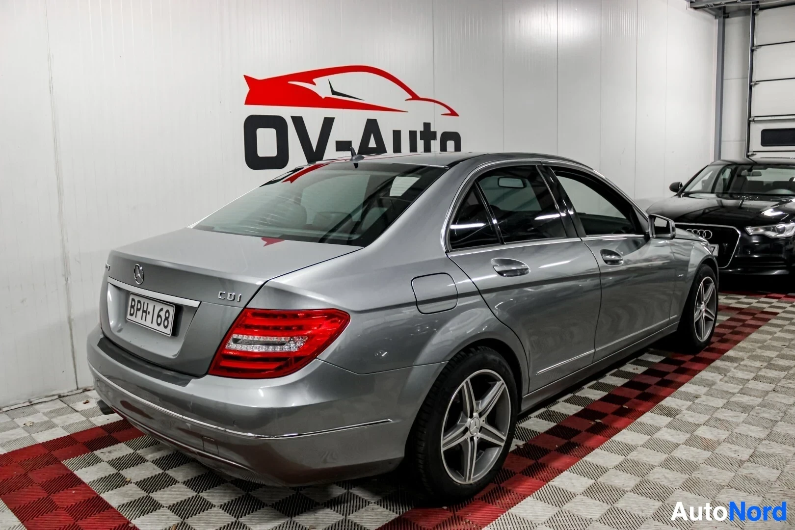 Takaviisto: Harmaa Mercedes-Benz C-sarja, rekisterinumero, kuvattuna takaa ja oikealta sivulta kohti vasenta. Ajoneuvo on pysäköity sisätiloihin OV-Auto-logolla var