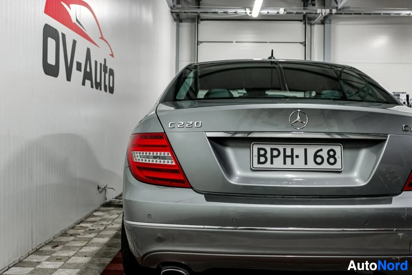 Takaa: Mercedes-Benz C-sarjan takapää, rekisterinumero, on kuvattu sisätiloissa OV-Auto-logolla varustetun seinän vieressä. Takavalot ja takaluukun C220-merkki