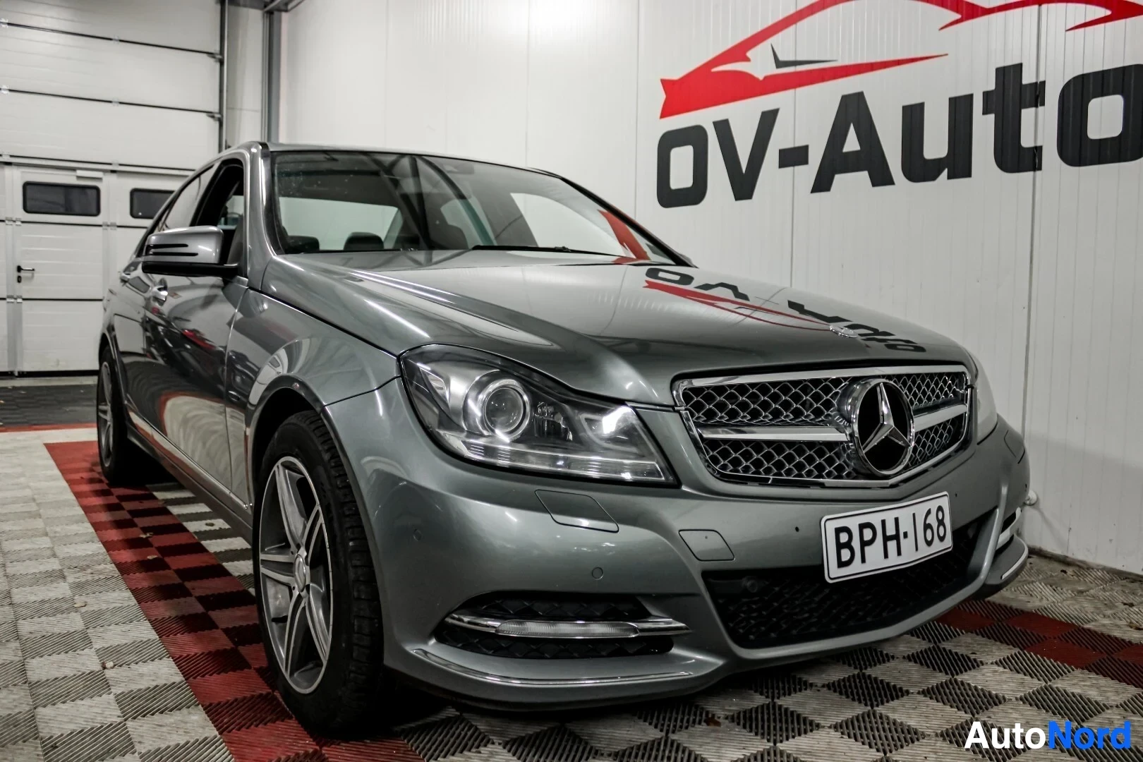 Etuviisto, nokka oikealle: Harmaa Mercedes-Benz C-sarja, rekisterinumero, kuvattuna edestä ja vasemmalta sivulta kohti oikeaa. Ajoneuvo on pysäköity sisätiloihin OV-Auto-lo
