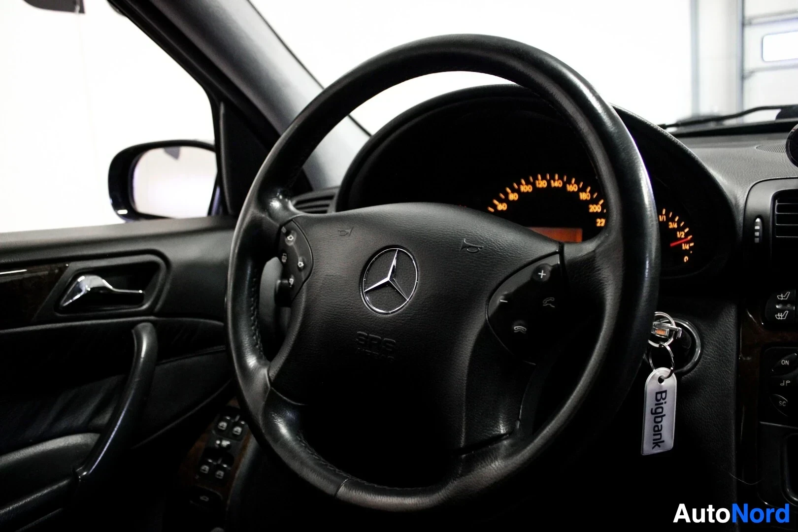Yksityiskohta: Lähikuva auton ohjauspyörästä ja mittaristosta. Ohjauspyörässä on Mercedes-Benz-logo ja useita painikkeita. Avaimet ovat virtalukossa.
